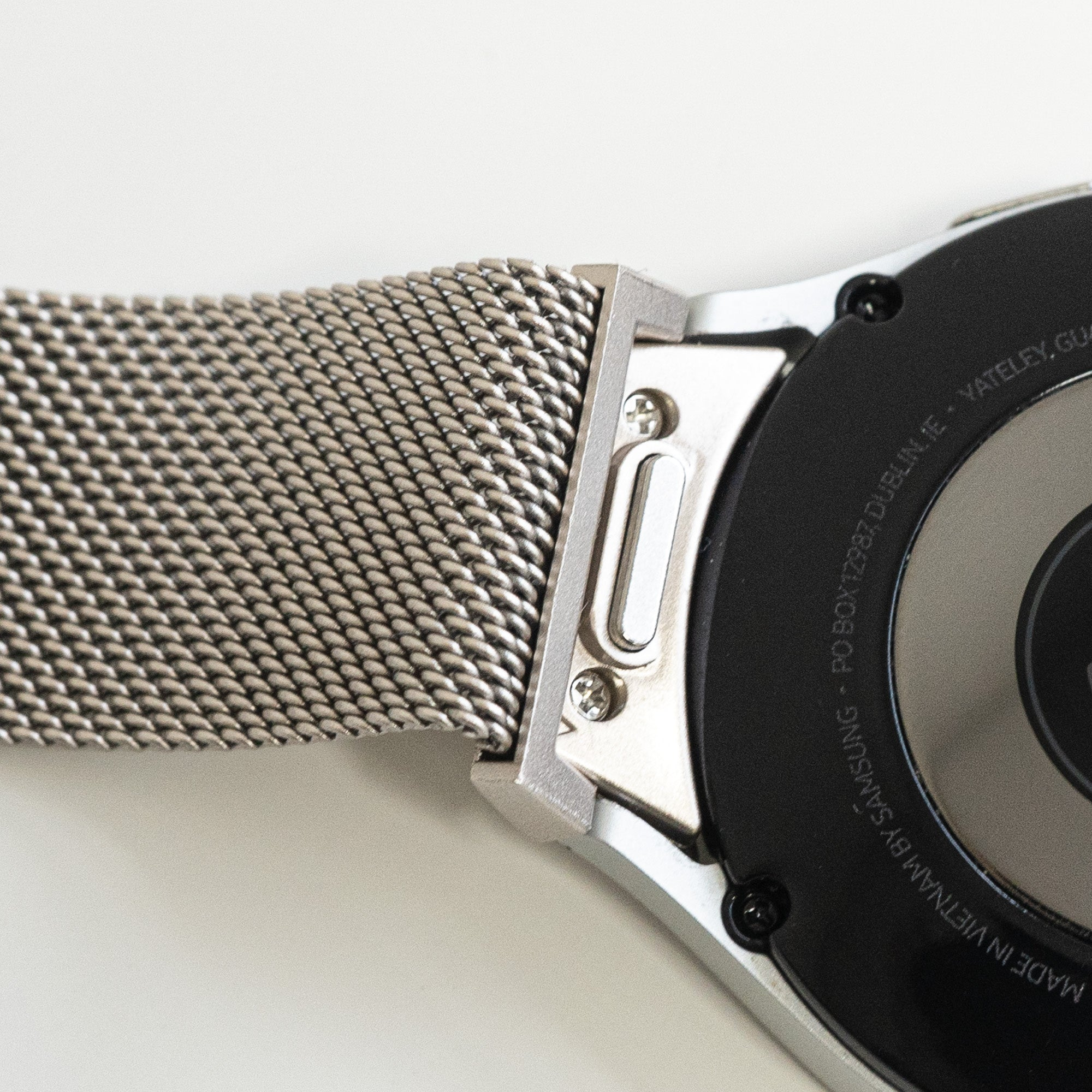Nahaufnahme einer silbernen Uhr und eines Armbands. Das Armband ist aus Mesh. Die Uhr hat eine schwarze Rückseite und silberne Verzierungen.
