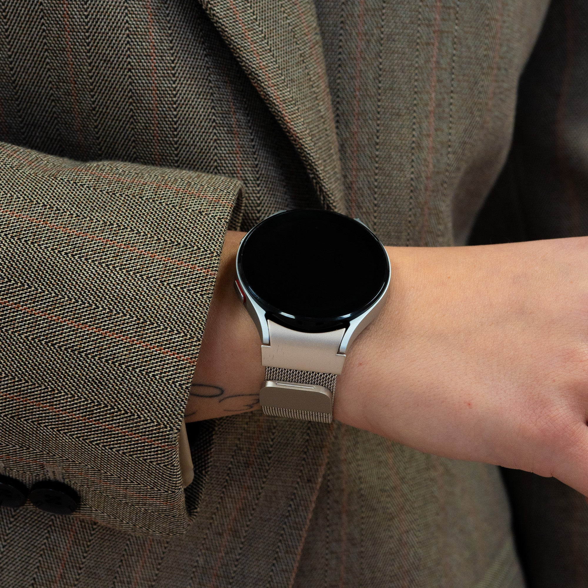 Eine Person trägt eine silberne Uhr mit schwarzem Bildschirm. Sie trägt eine braune Anzugjacke. Die Uhr ist an ihrem Handgelenk.