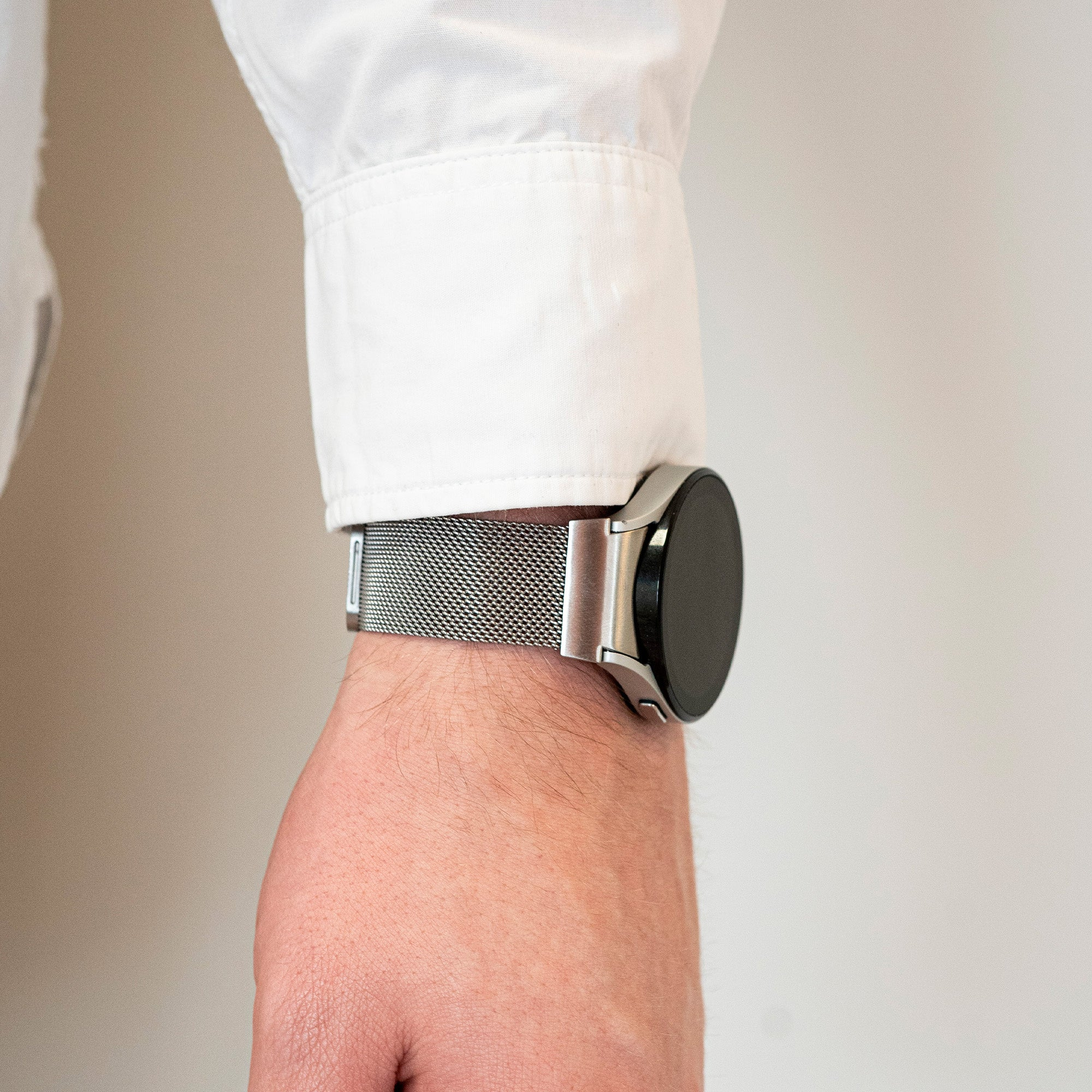 Das Handgelenk einer Person mit einer silbernen Uhr. Über dem Handgelenk ist ein weißer Hemdärmel zu sehen. Der Hintergrund ist weiß.