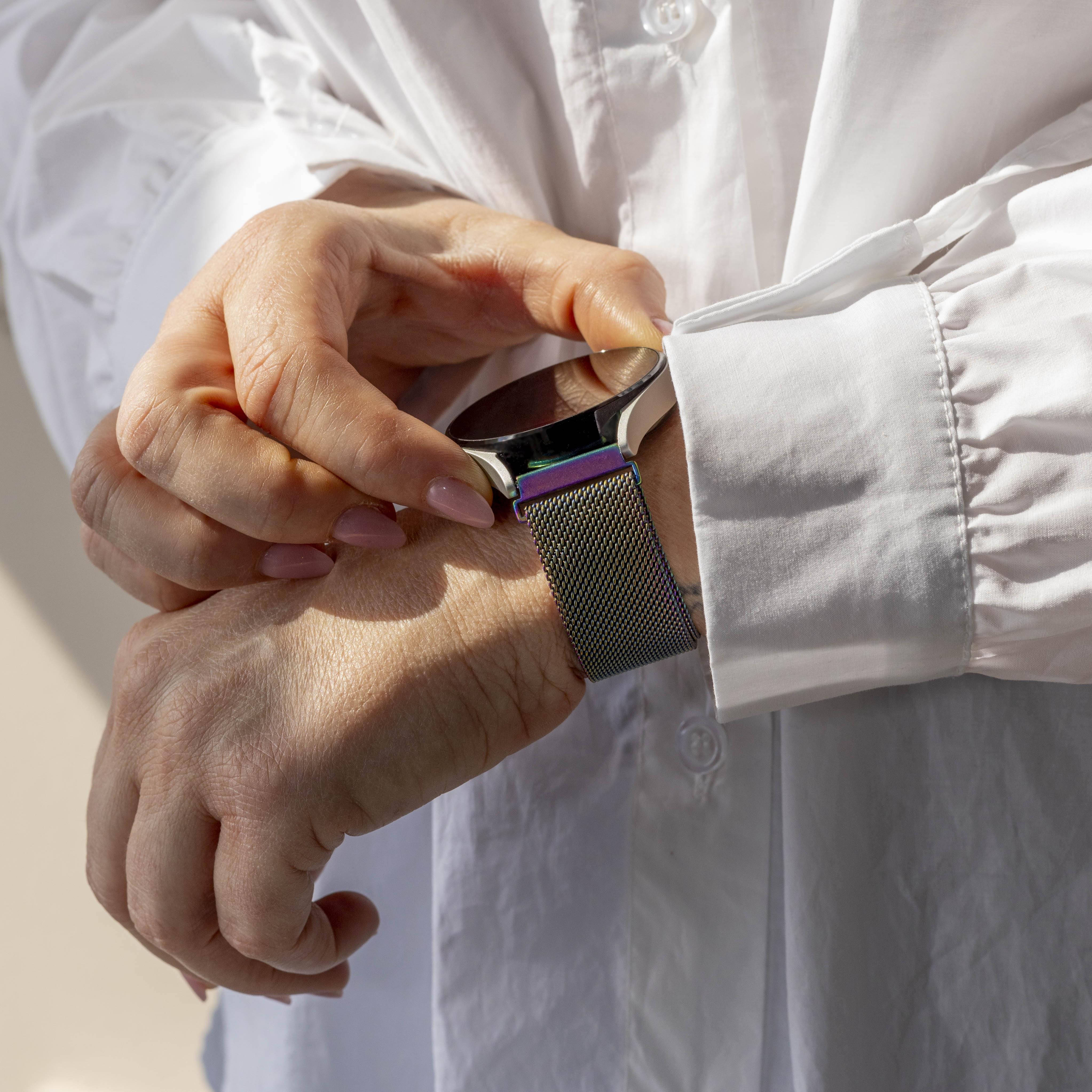 Eine Person, die eine Smartwatch an ihrem Handgelenk einstellt. Sie trägt ein weißes Hemd. Die Uhr hat ein buntes Armband.