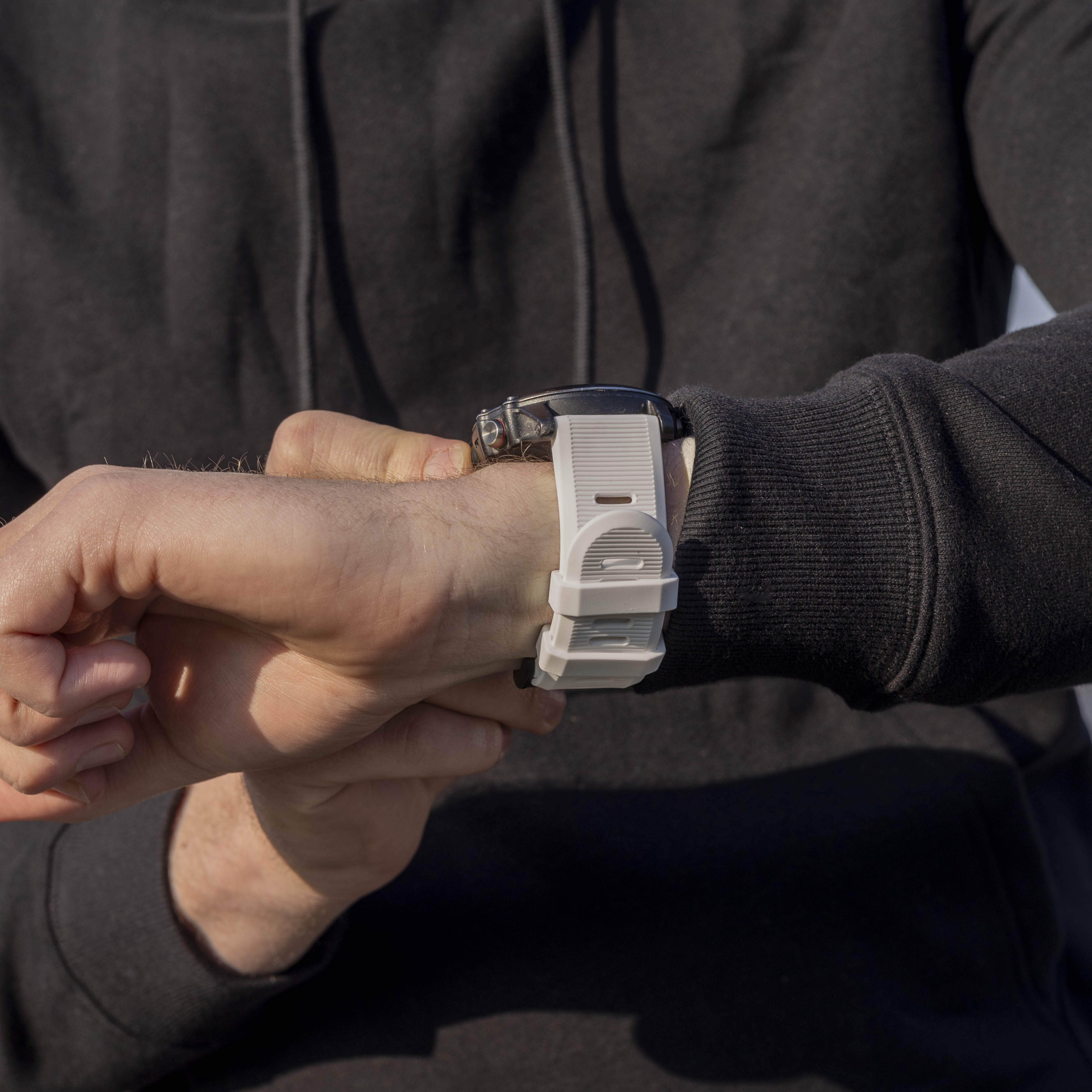 Eine Person mit schwarzem Kapuzenpullover betrachtet eine weiße Smartwatch an ihrem Handgelenk. Die Uhr hat ein schwarzes Zifferblatt.