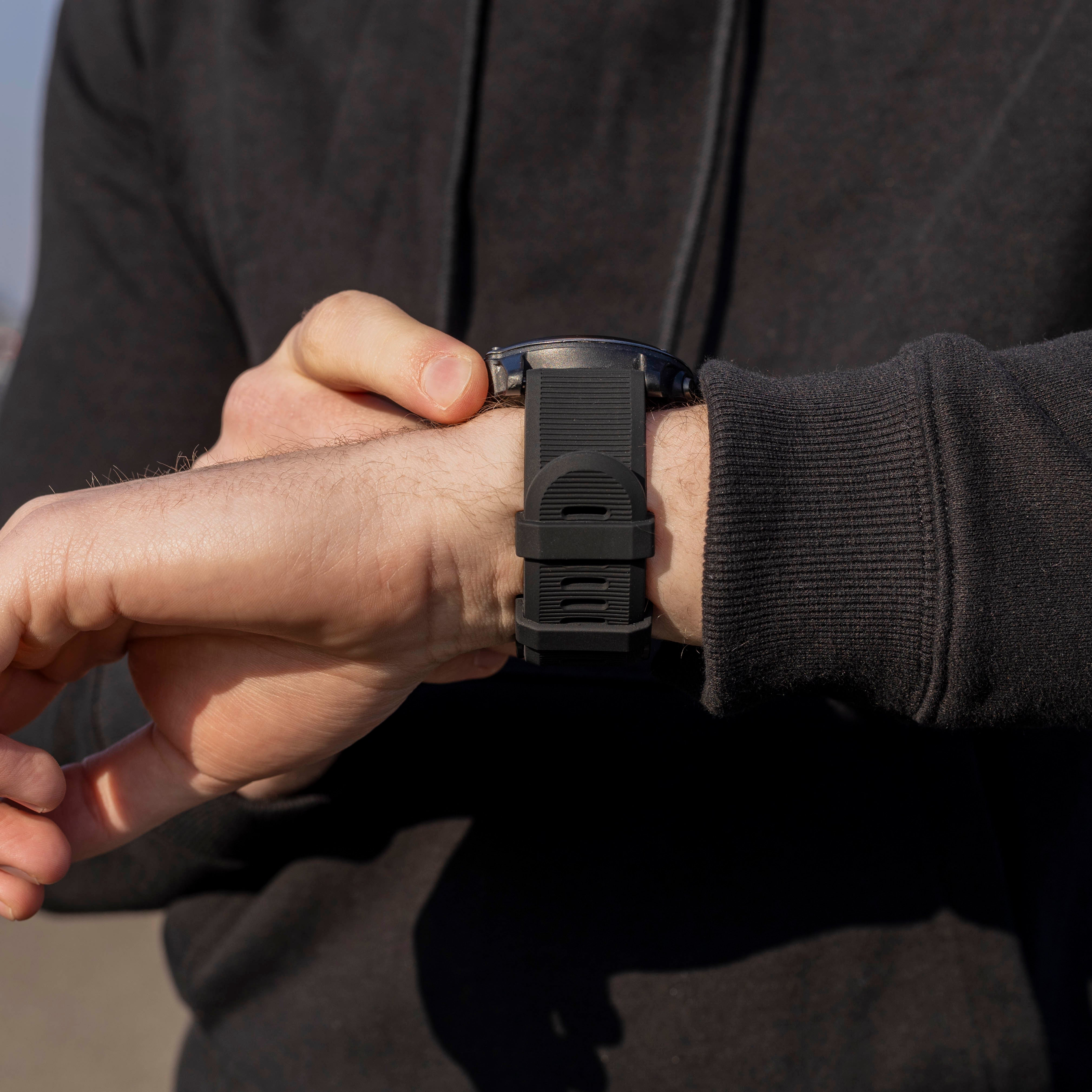 Eine Person, die eine schwarze Smartwatch am Handgelenk trägt und sie einstellt. Die Person trägt einen schwarzen Kapuzenpullover.