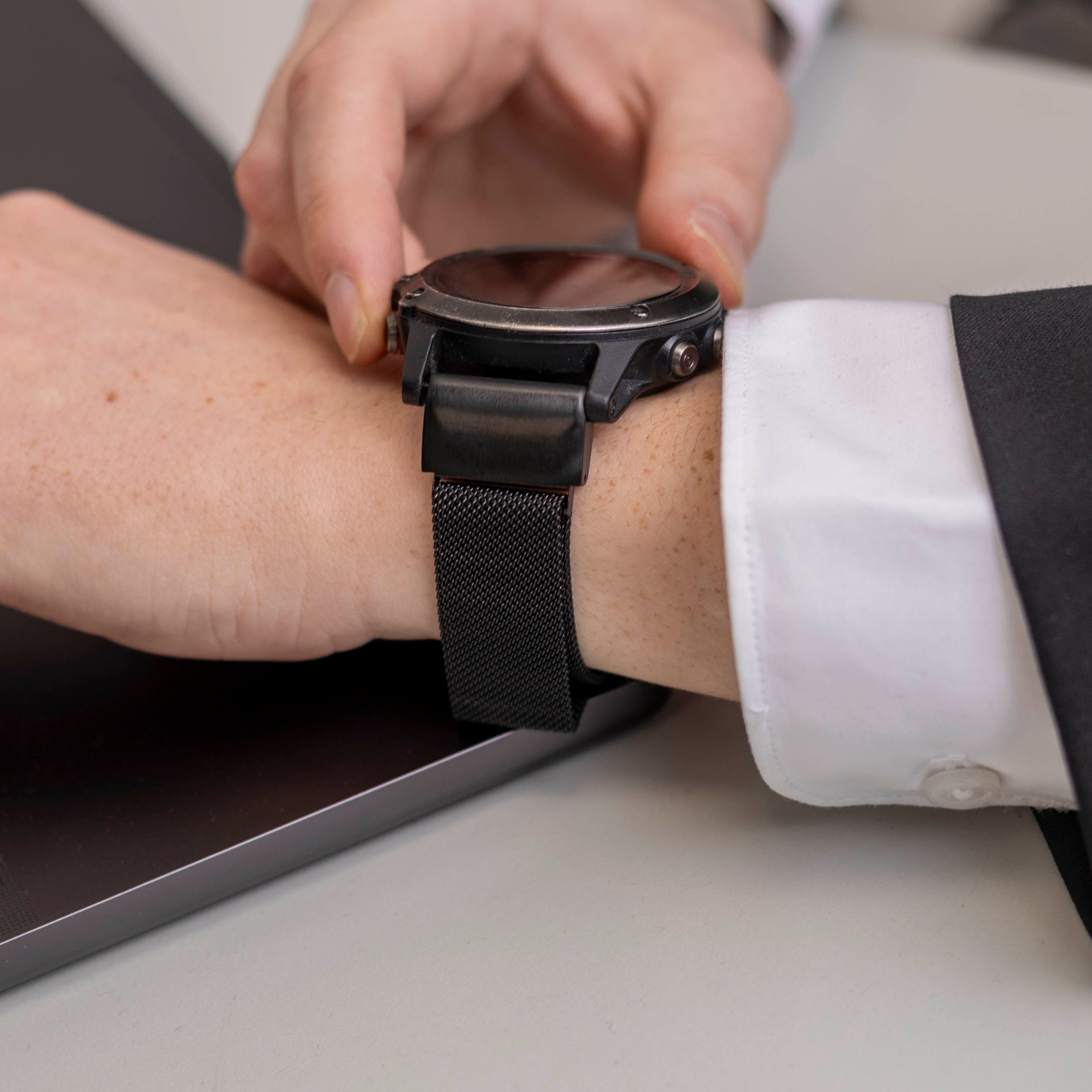 Das Handgelenk einer Person mit einer schwarzen Uhr und einem Armband. Die Hand der Person stellt die Uhr ein.