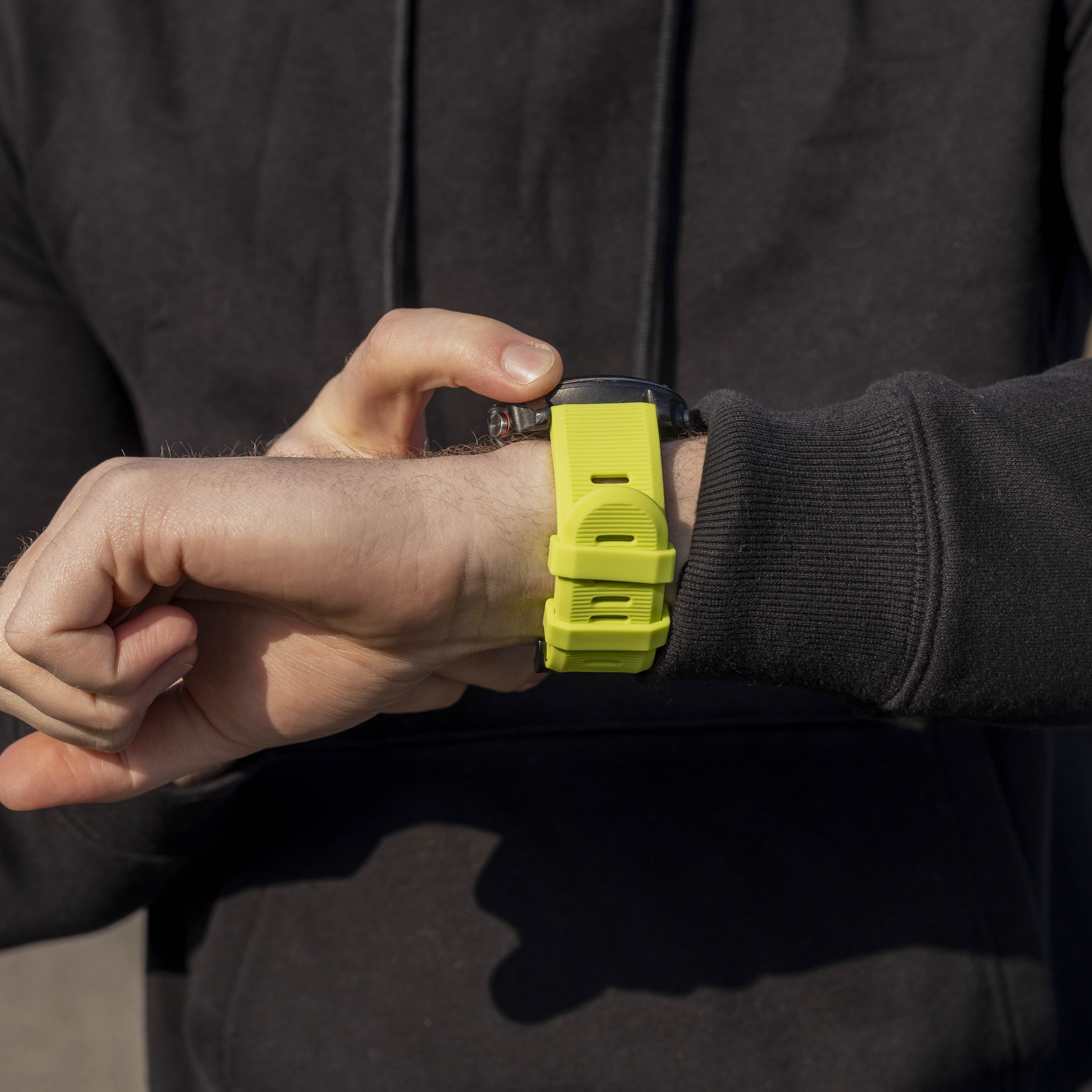 Eine Person mit schwarzem Kapuzenpullover stellt eine Smartwatch mit einem leuchtend grünen Armband ein.