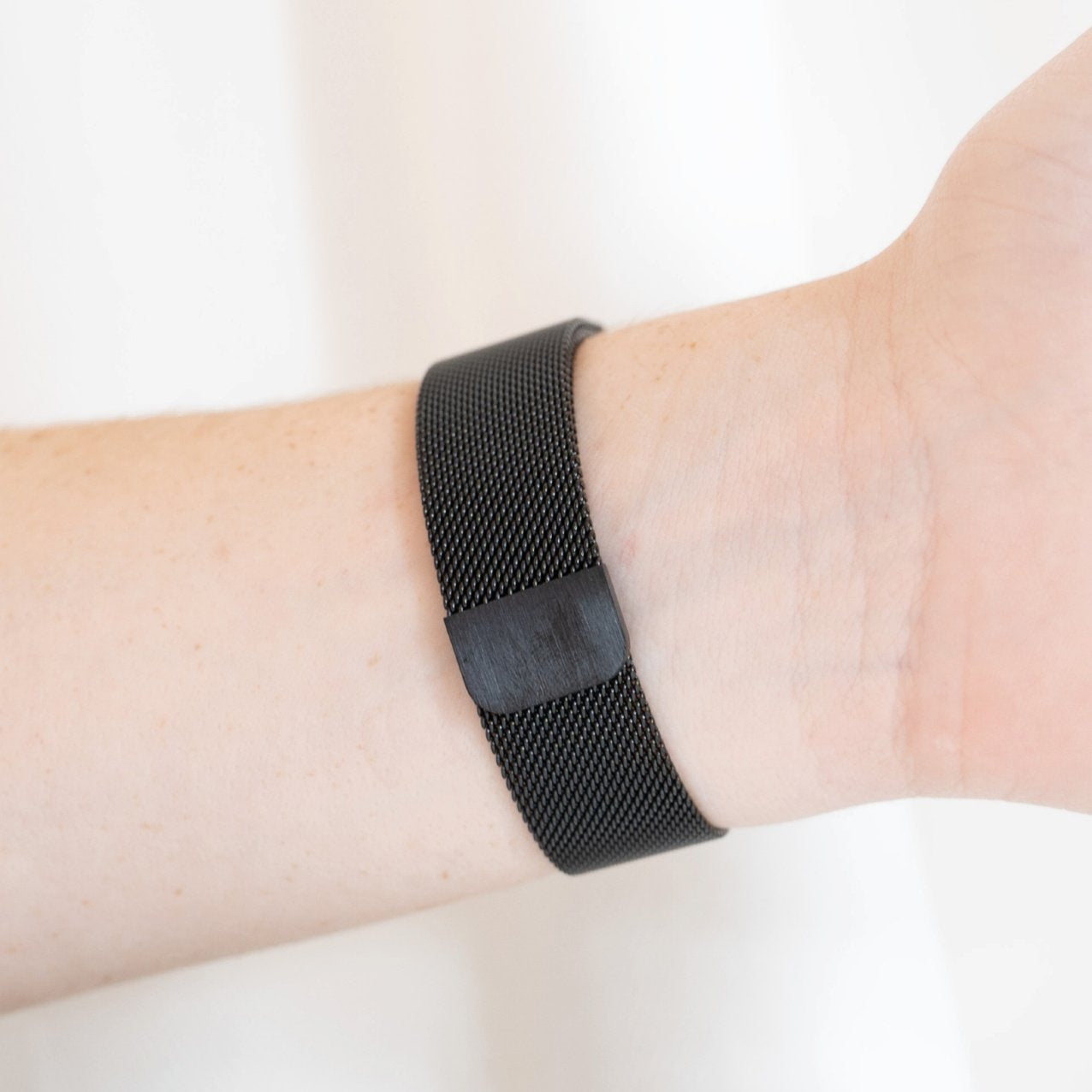 Ein Handgelenk, das ein schwarzes Mesh-Uhrenarmband trägt. Das Band ist um das Handgelenk befestigt. Die Haut ist hell.