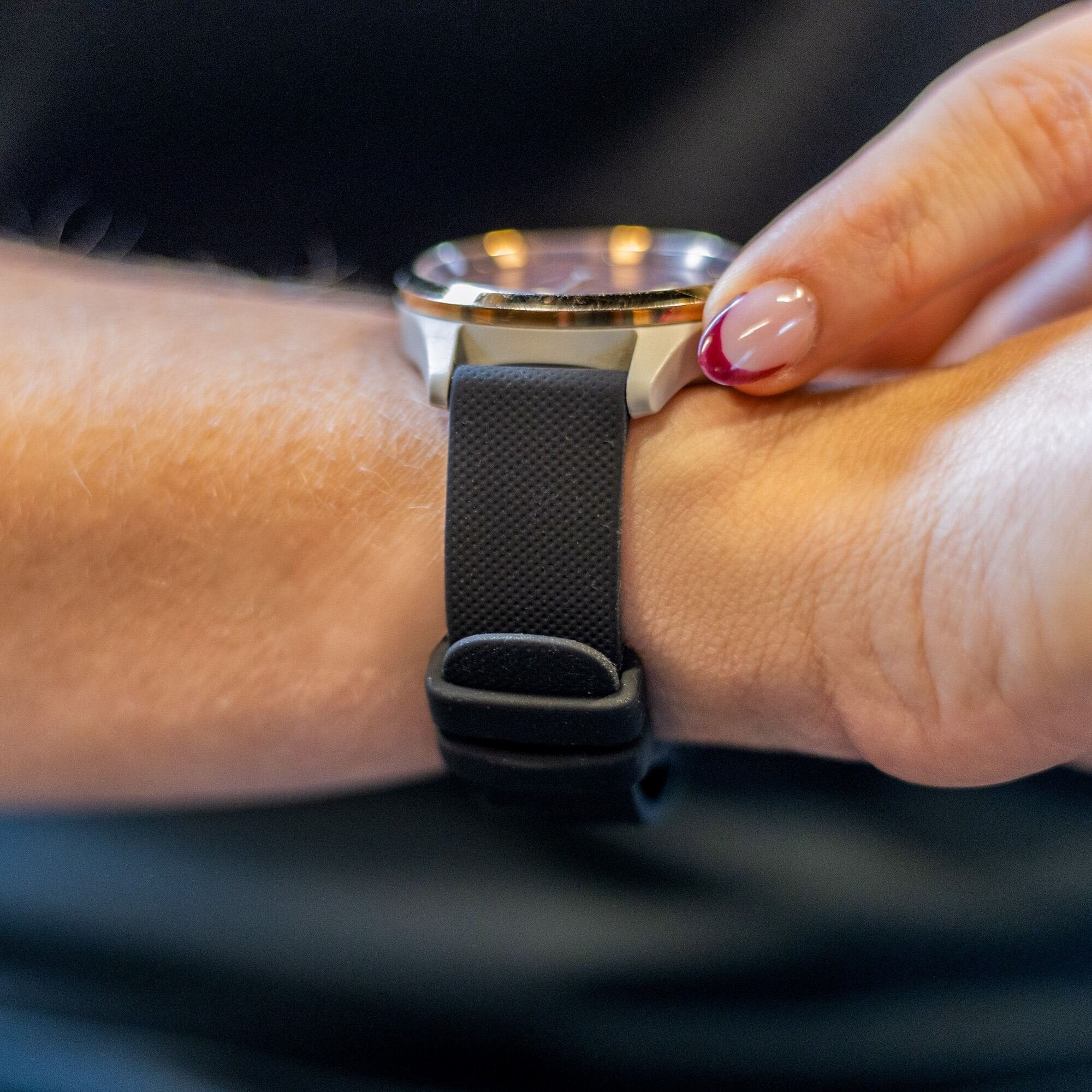 Handgelenk mit schwarzer Uhr. Eine Hand mit lackiertem Nagel justiert die Uhr.