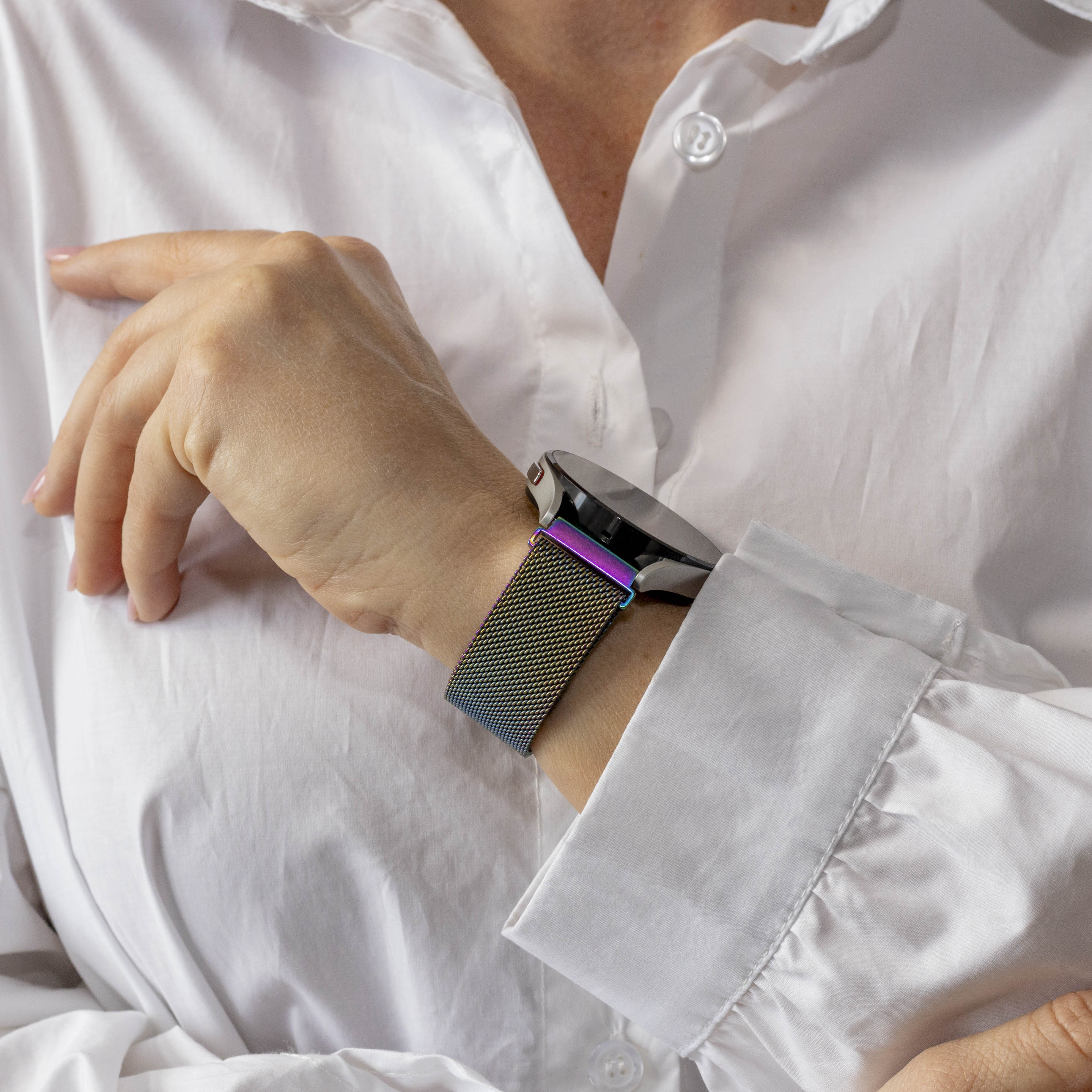 Das Handgelenk einer Person mit einem bunten Uhrenarmband ist sichtbar. Sie trägt ein weißes Hemd.