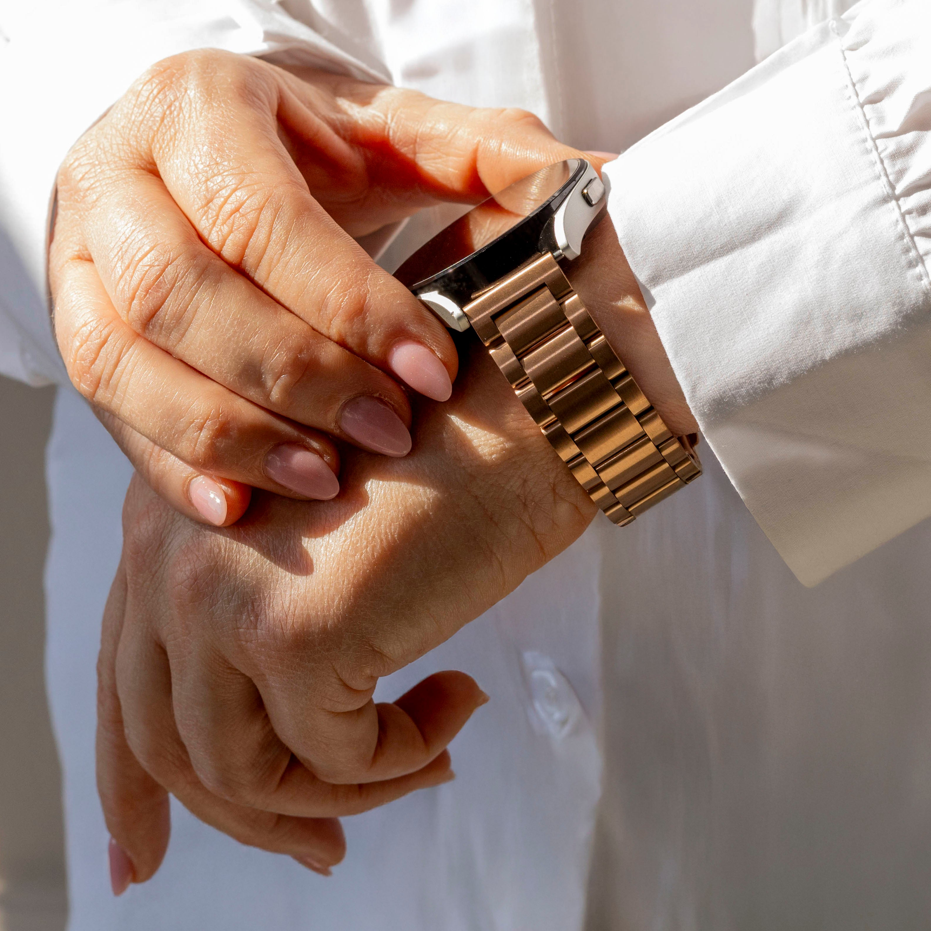 Eine Person trägt eine goldene Uhr am Handgelenk. Sie trägt ein weißes Hemd. Das Zifferblatt ist schwarz.