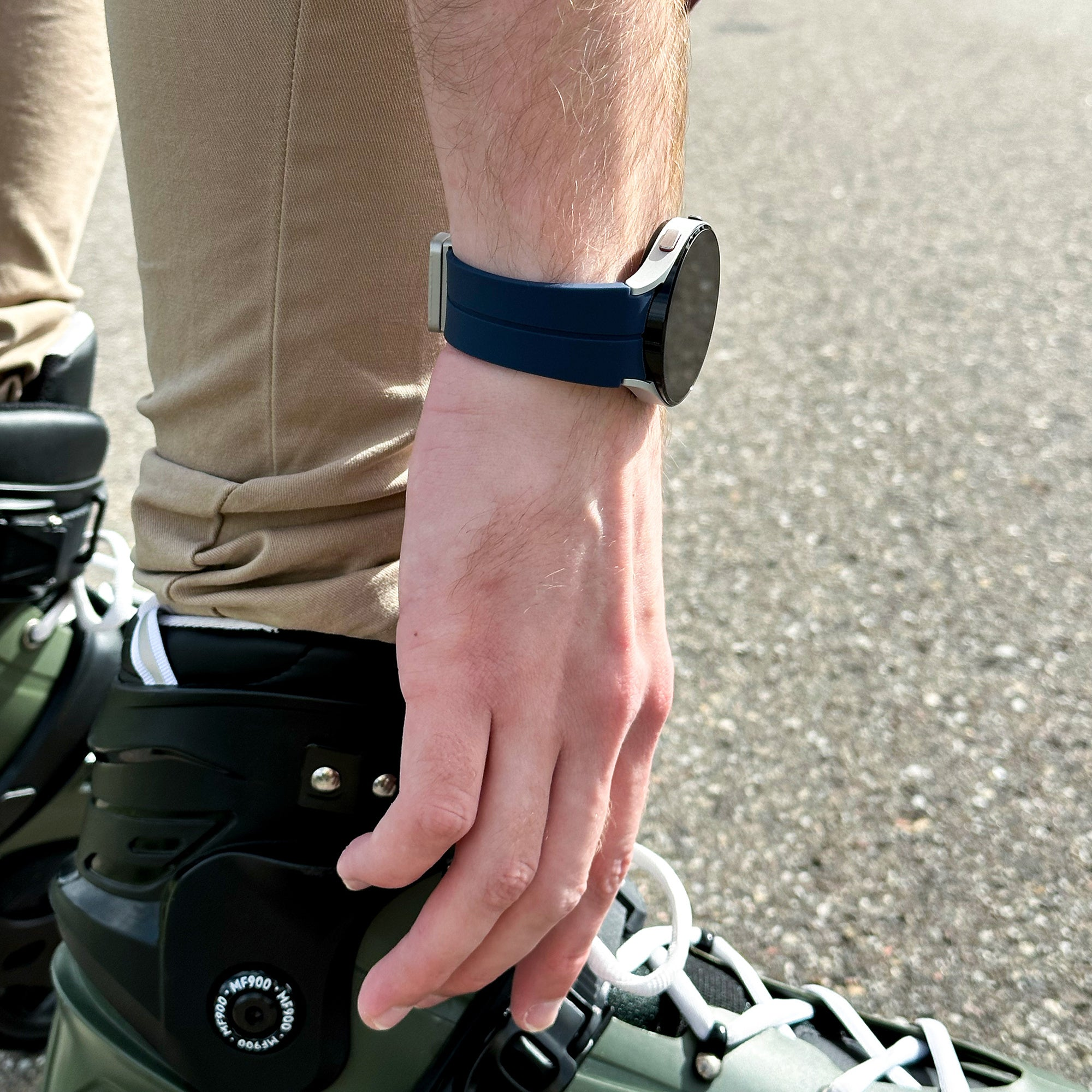 Eine Person trägt Rollschuhe und eine Smartwatch mit blauem Armband. Die Hand ruht auf dem Rollschuh.