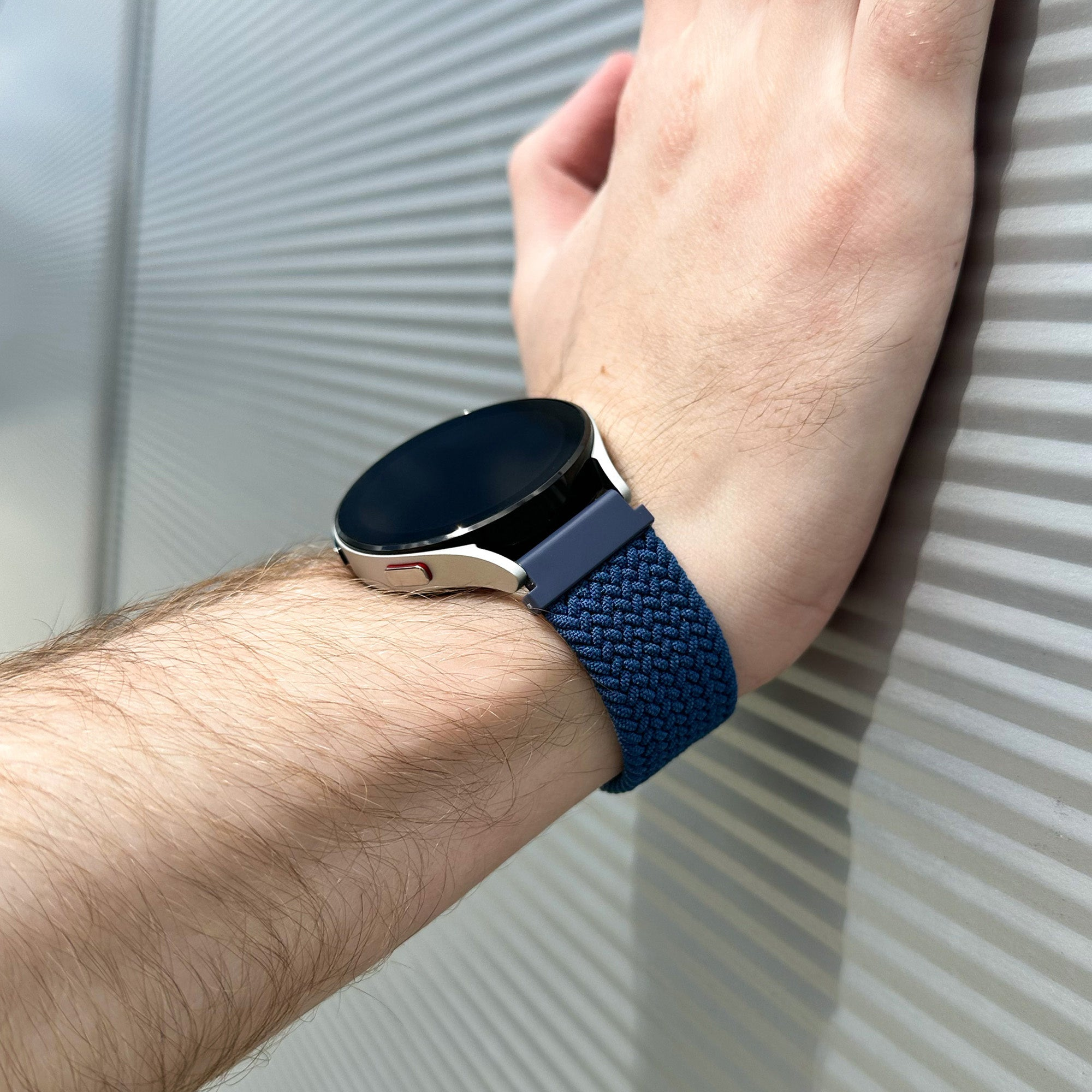 Handgelenk mit blauer Uhr und Armband vor geriffelter Wand.