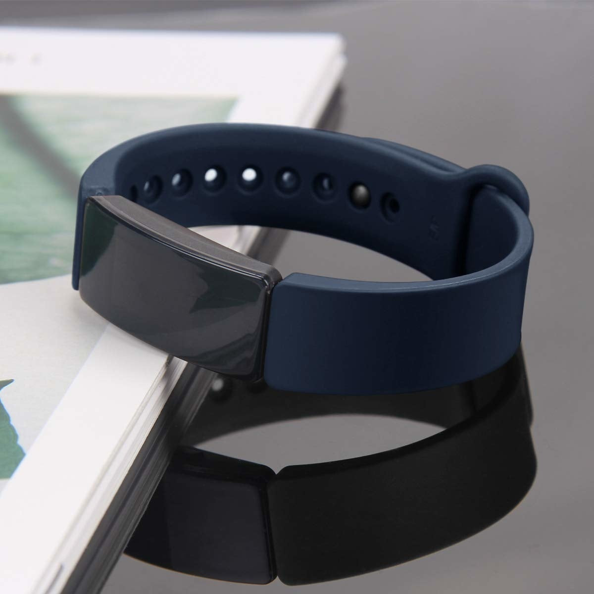 Ein dunkelblauer Fitness-Tracker auf einem Buch. Der Tracker hat einen schwarzen Bildschirm und ein dunkelblaues Band. Der Hintergrund ist grau.