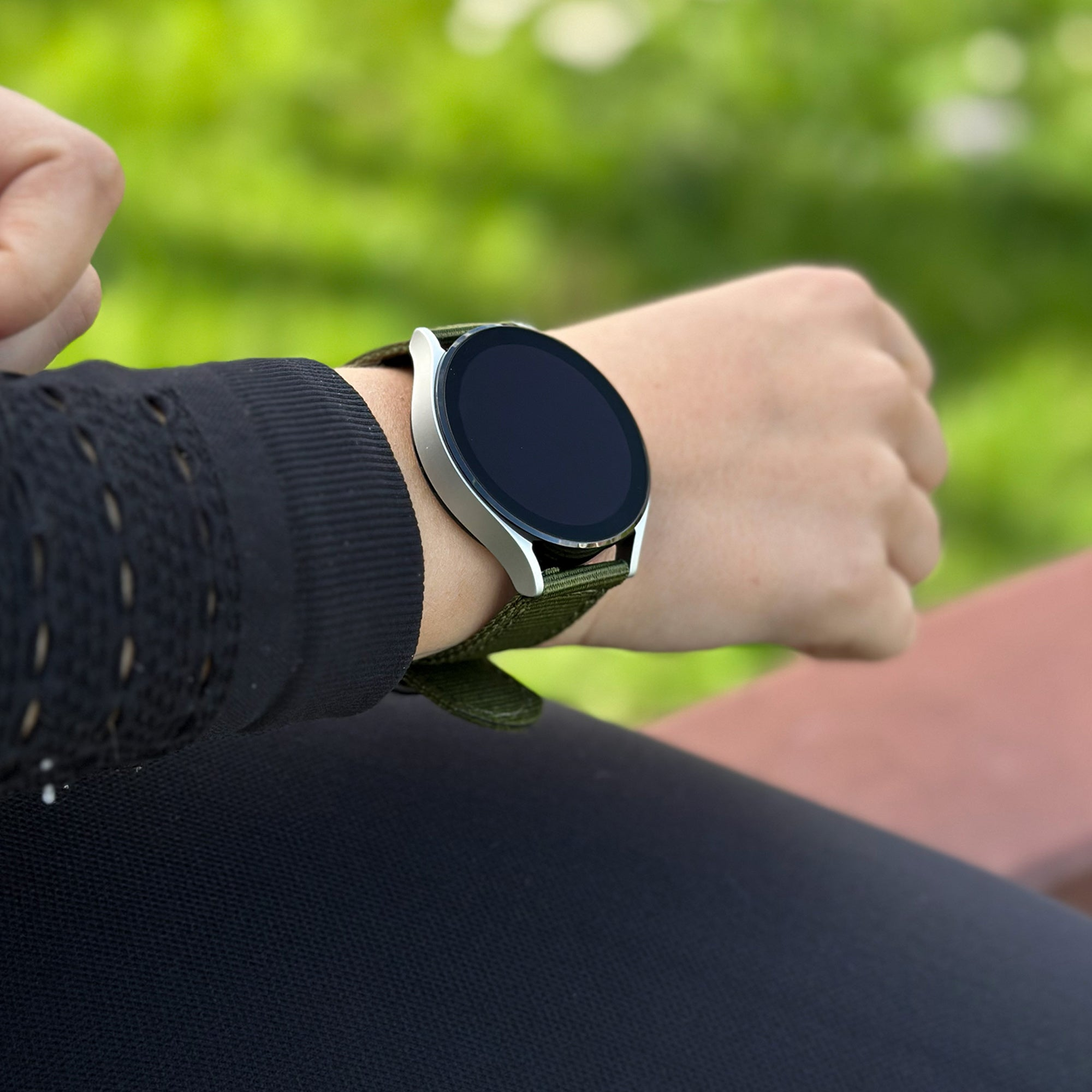 Eine Person, die eine Smartwatch mit grünem Armband trägt. Der Hintergrund ist unscharf grün.