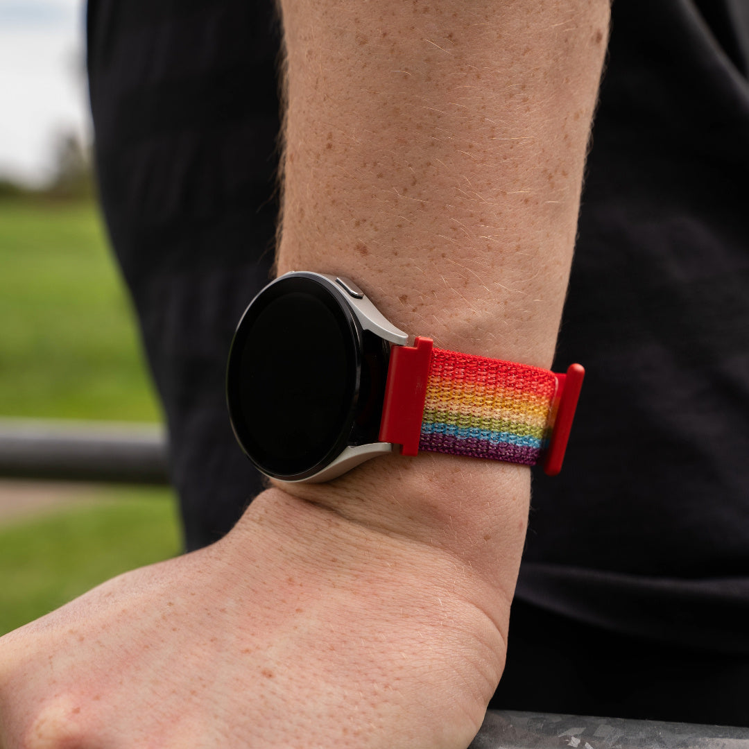 Handgelenk mit Smartwatch. Die Uhr hat ein Regenbogenarmband. Das Handgelenk ist hellhäutig.