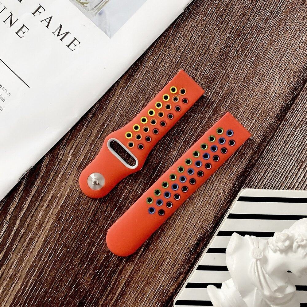 Zwei orangefarbene Uhrenarmbänder mit farbigen Löchern auf einer Holzoberfläche. Eines hat gelbe Löcher, das andere blaue, grüne und gelbe.