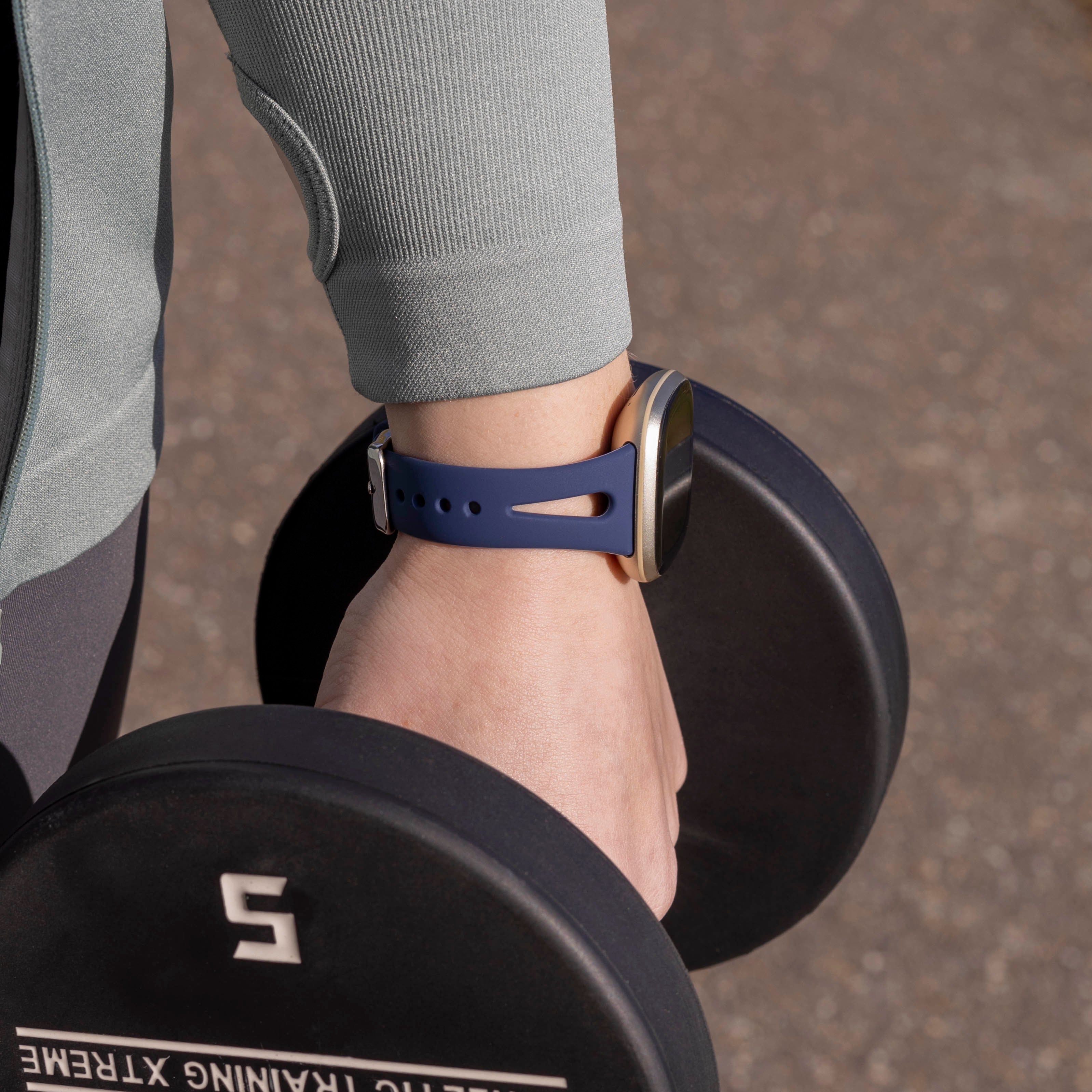 Eine Person hält eine Hantel. Eine Smartwatch befindet sich am Handgelenk. Die Person trägt einen grauen Pullover. Der Hintergrund ist unscharf.