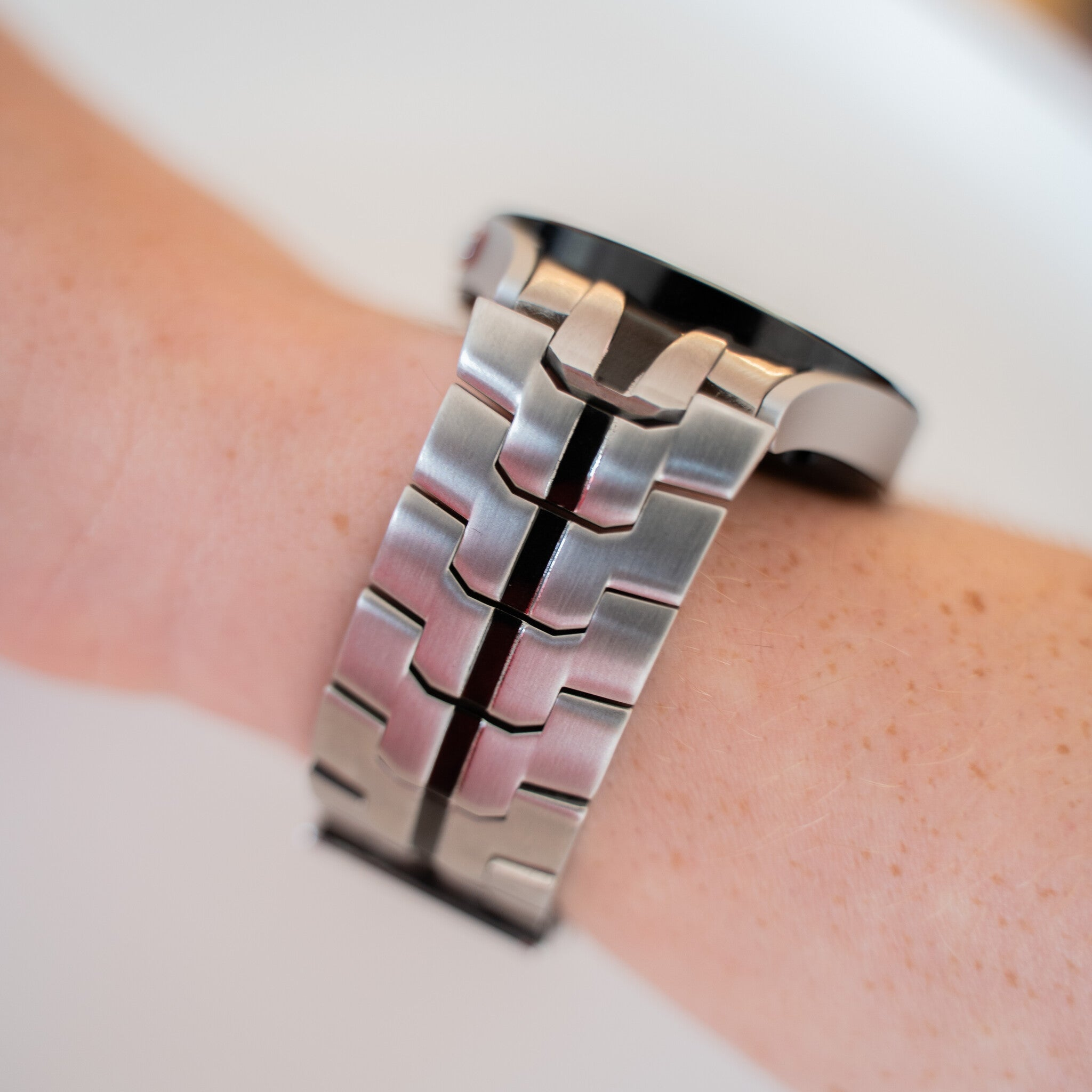 Eine silberne Uhr mit Metallarmband befindet sich am Handgelenk einer Person. Die Haut ist hell mit Sommersprossen. Der Hintergrund ist weiß.