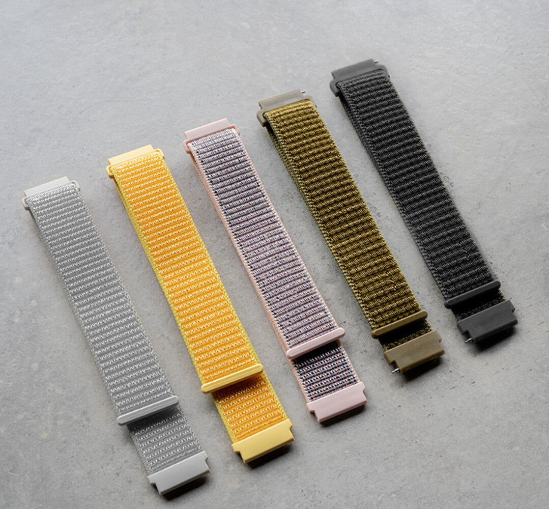 Fünf bunte Uhrenarmbänder sind ausgelegt. Sie sind grau, gelb, rosa, oliv und schwarz. Alle haben Metallschnallen.