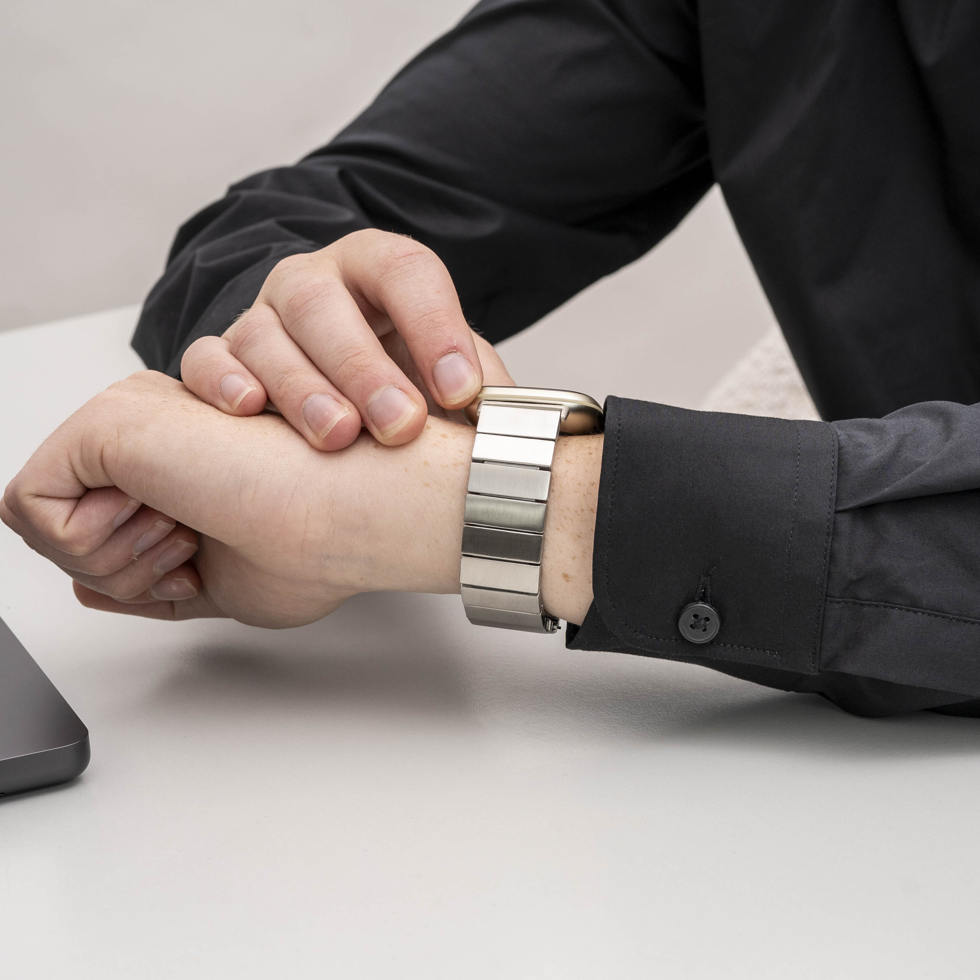 Die Hand einer Person, die eine silberne Uhr an ihrem Handgelenk einstellt. Schwarzes Hemd ist sichtbar.