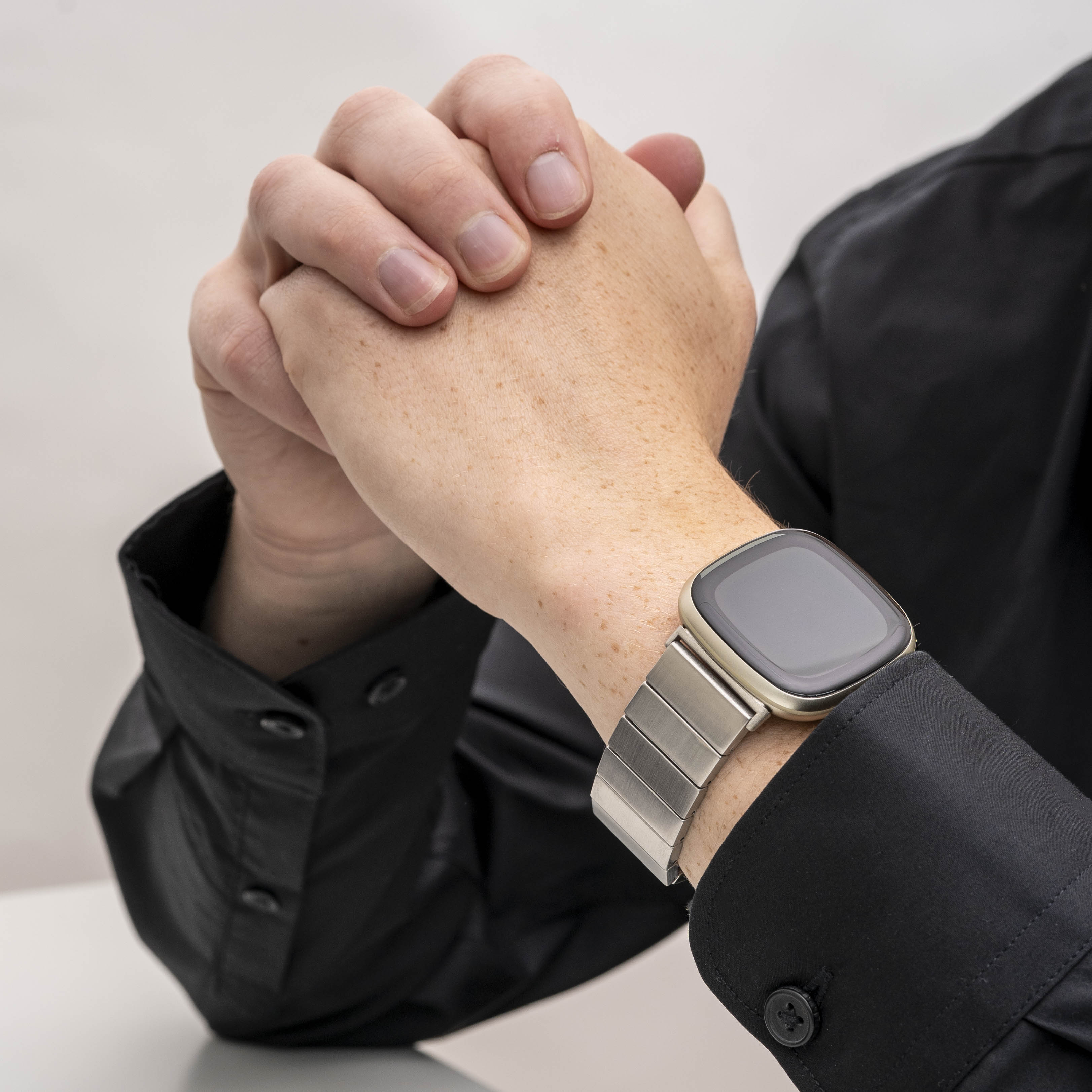 Nahaufnahme von Händen mit Smartwatch. Die Person trägt ein schwarzes Hemd. Die Uhr hat ein silbernes Armband und einen schwarzen Bildschirm.