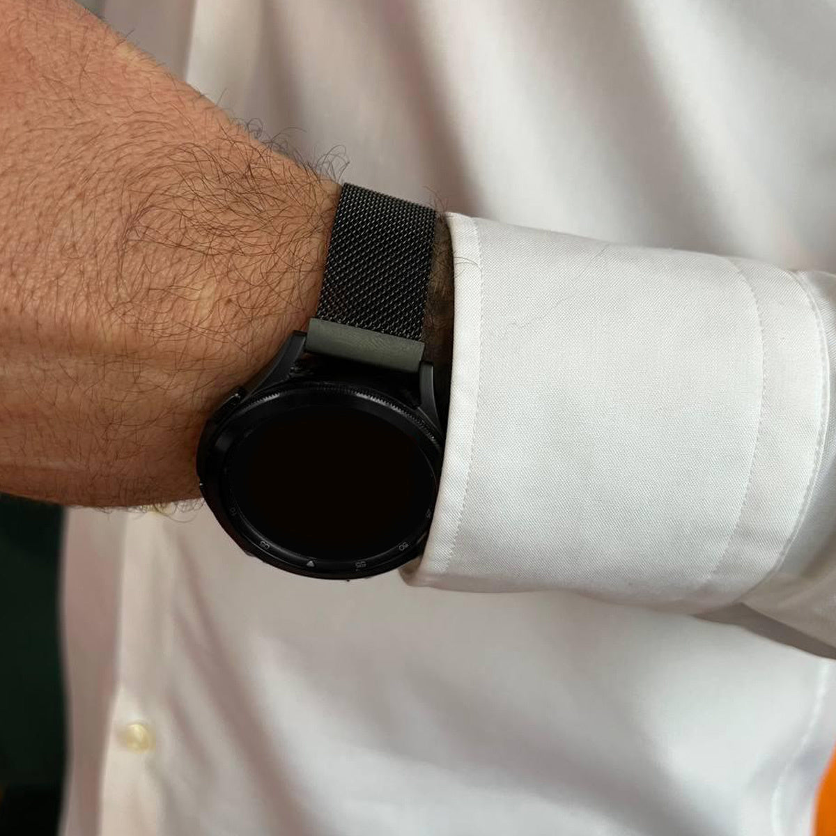 Der Arm einer Person mit einer schwarzen Smartwatch. Die Uhr befindet sich an einem Handgelenk, das ein weißes Hemd trägt. Die Uhr hat ein schwarzes Band.