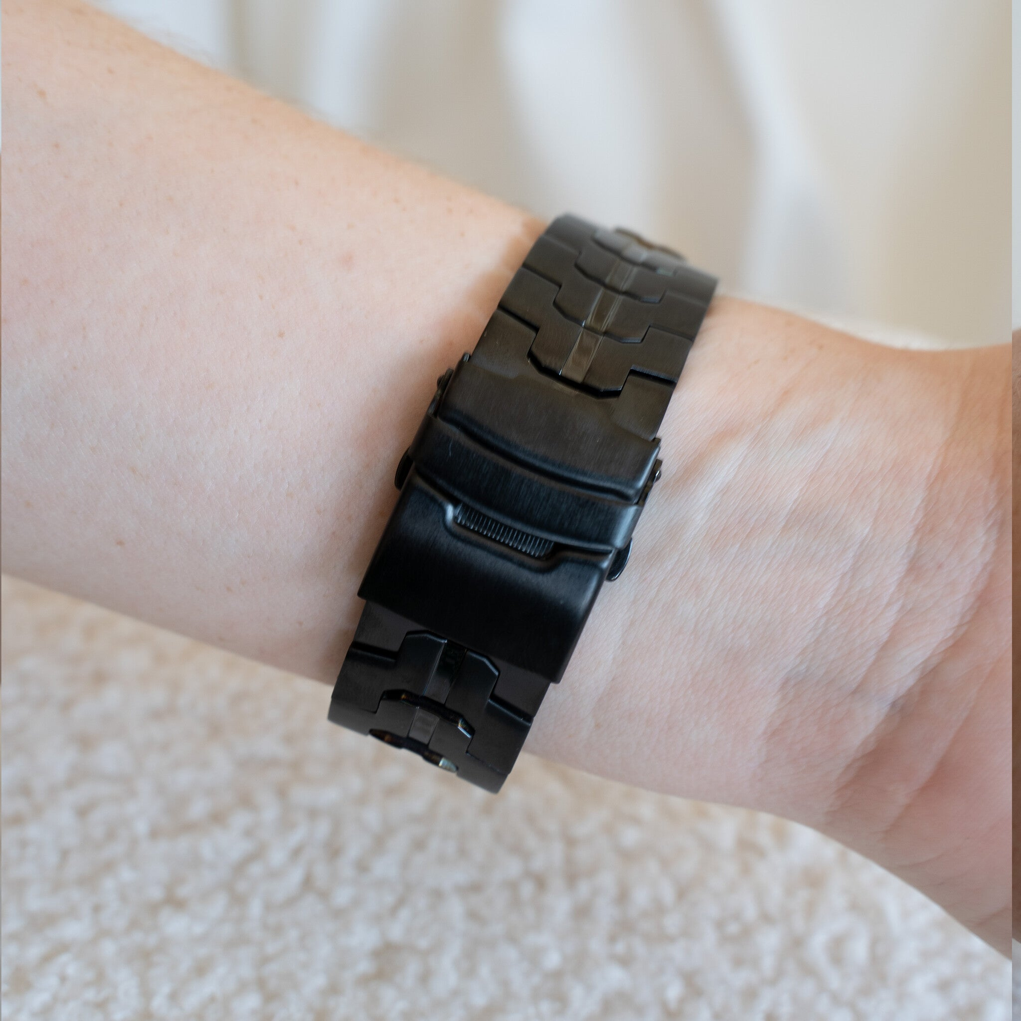 Ein Handgelenk mit einer schwarzen Uhr. Die Haut ist hell mit kleinen Sommersprossen. Der Hintergrund ist weiß.