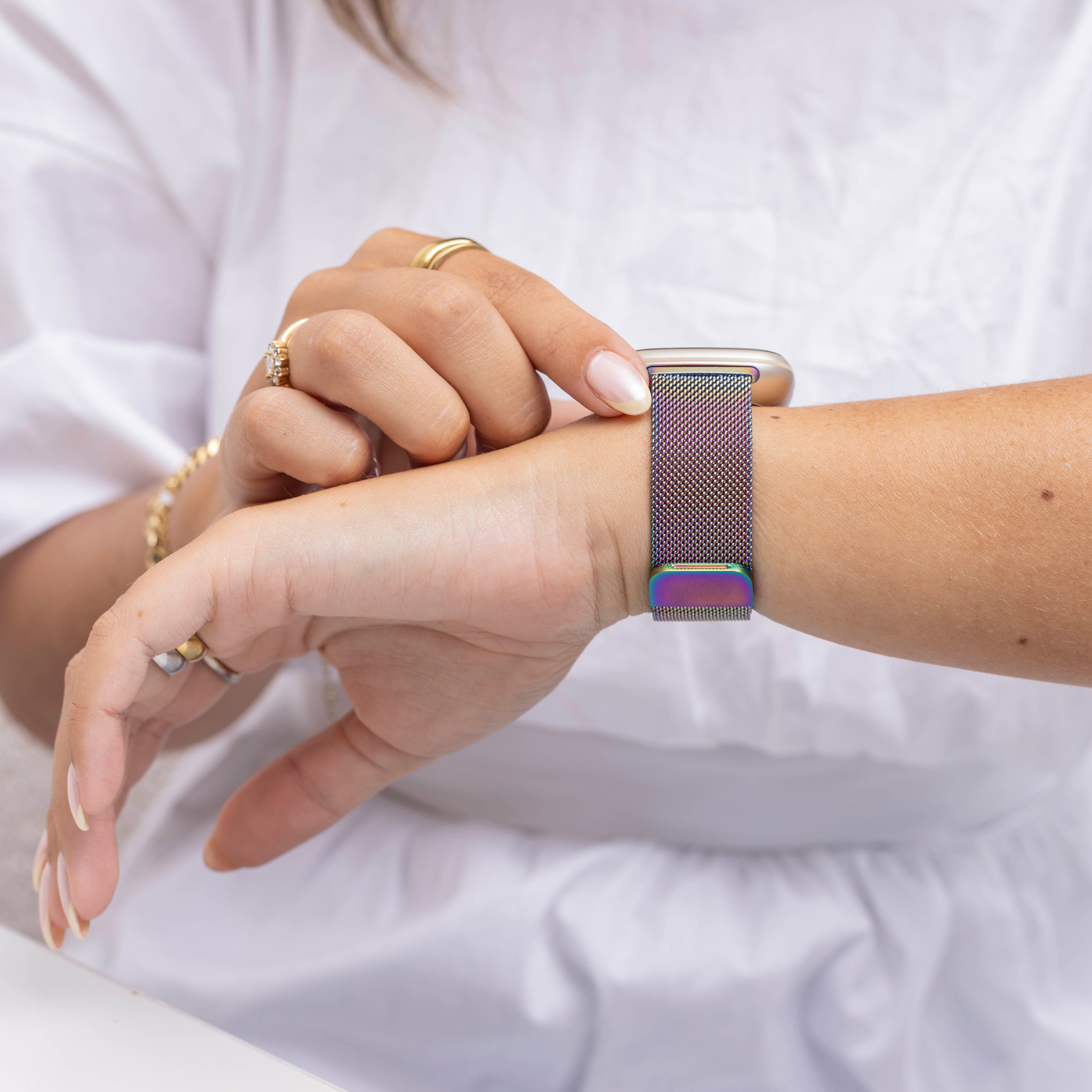 Handgelenk einer Person mit einer Uhr. Das Uhrenarmband ist irisierend. Die Person trägt Ringe und ein weißes Hemd.