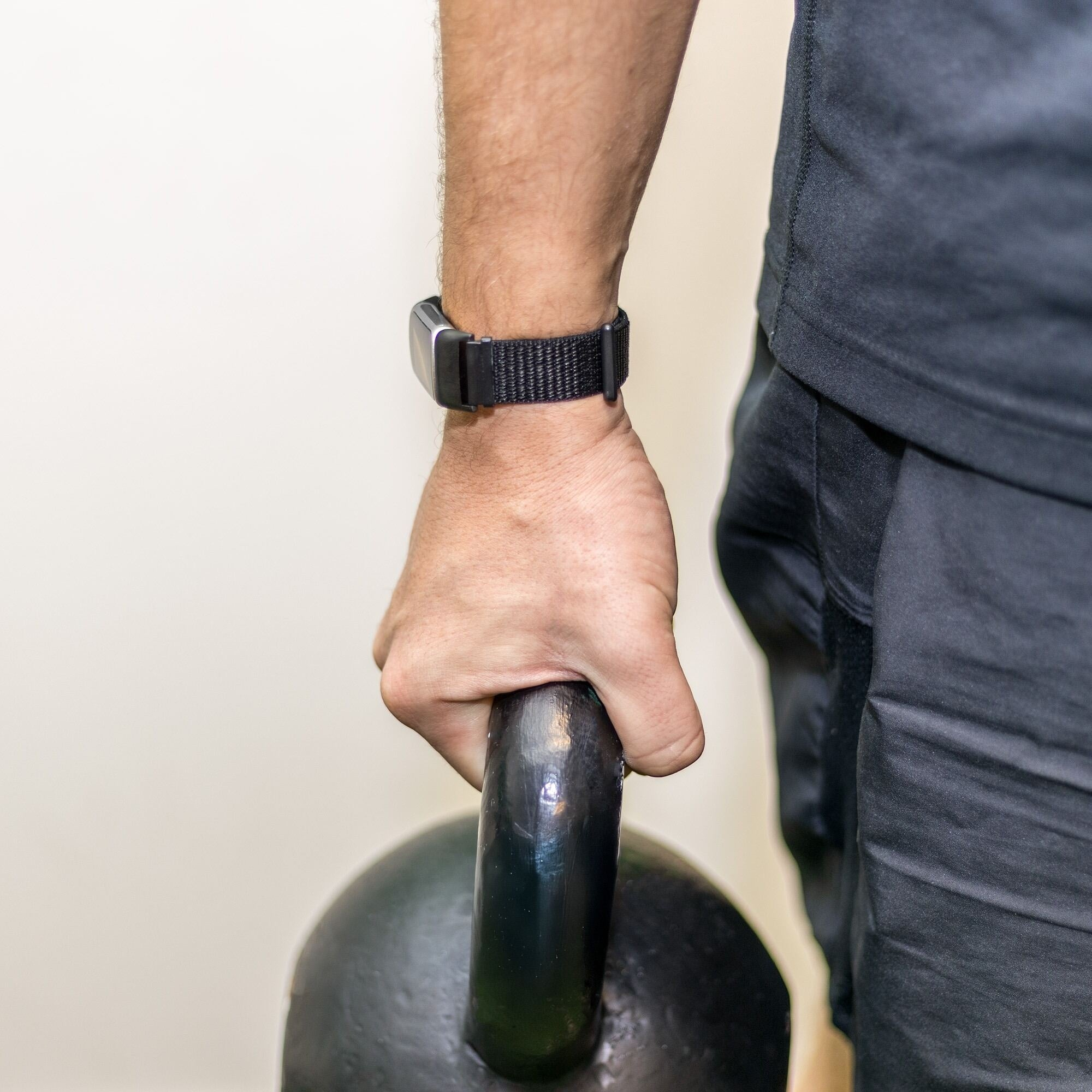 Die Hand einer Person hält eine schwarze Kettlebell. Am Handgelenk befindet sich eine Uhr. Die Person trägt schwarze Kleidung.