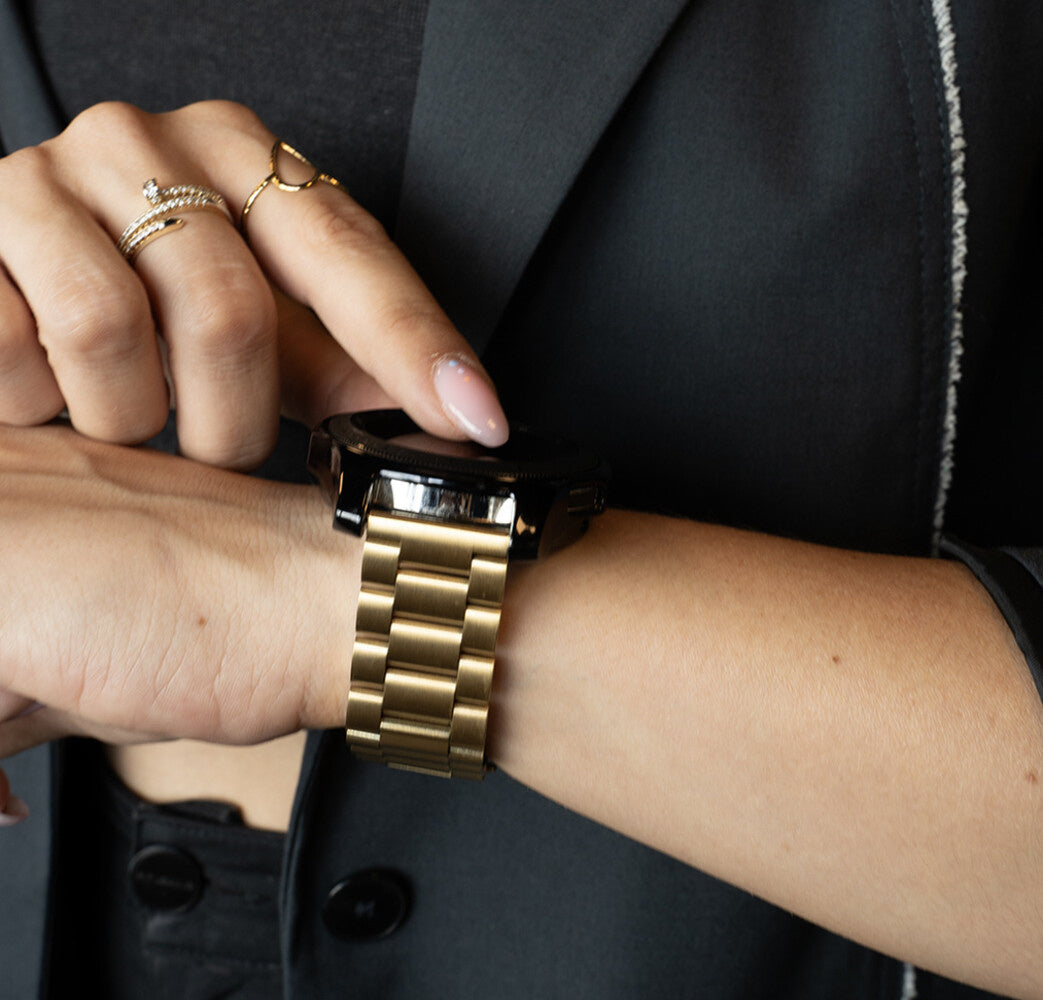 Eine Person mit Ringen berührt eine Smartwatch mit goldenem Armband. Die Person trägt einen schwarzen Blazer.