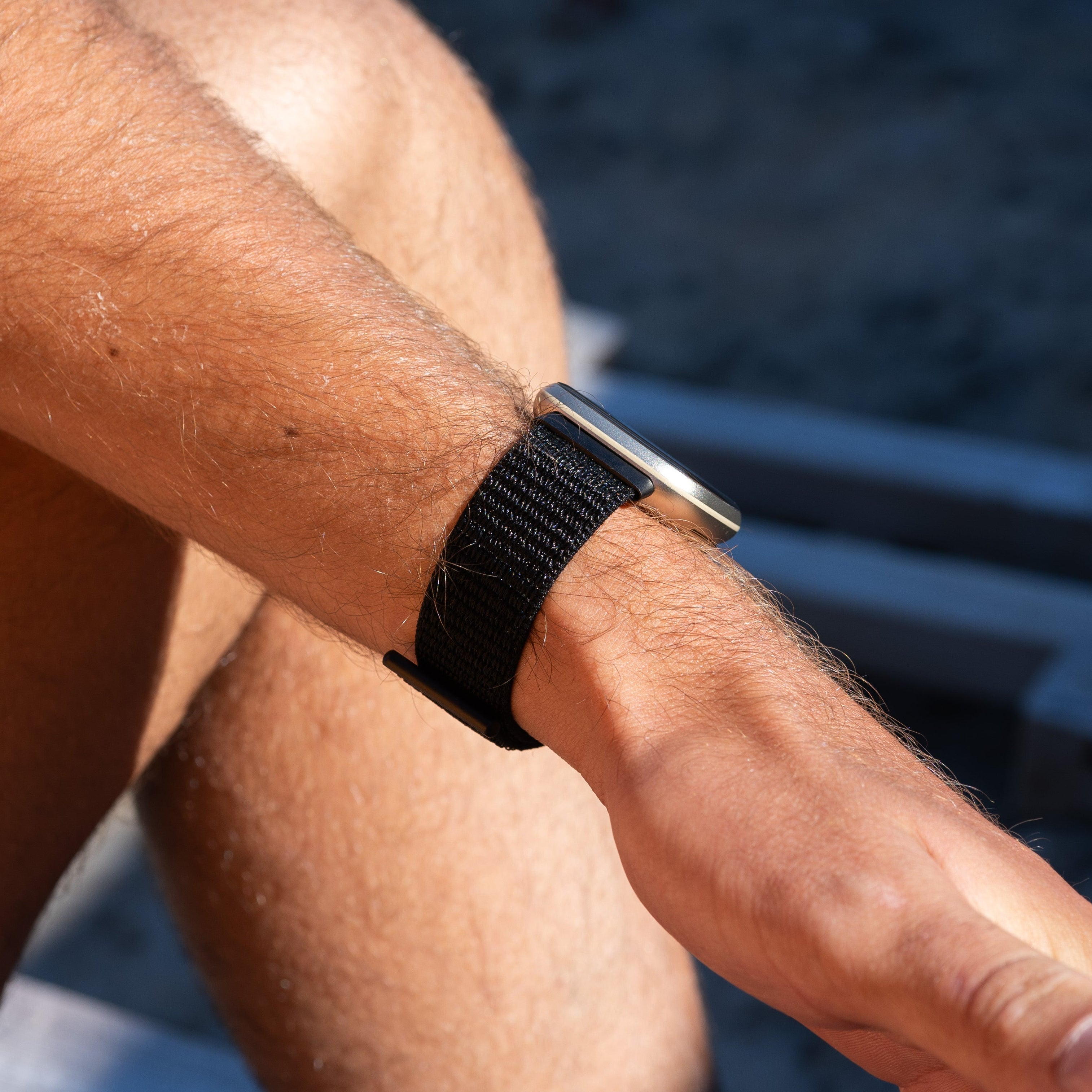 Arm einer Person mit einem schwarzen Uhrenarmband. Die Haut ist gebräunt, am Handgelenk ist eine Uhr.