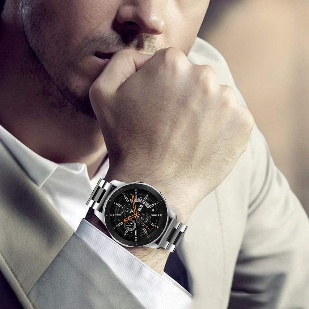 Mann, der eine silberne Armbanduhr trägt. Die Uhr hat ein schwarzes Zifferblatt mit orangefarbenen Akzenten. Der Mann trägt ein weißes Hemd und eine beige Anzugjacke.