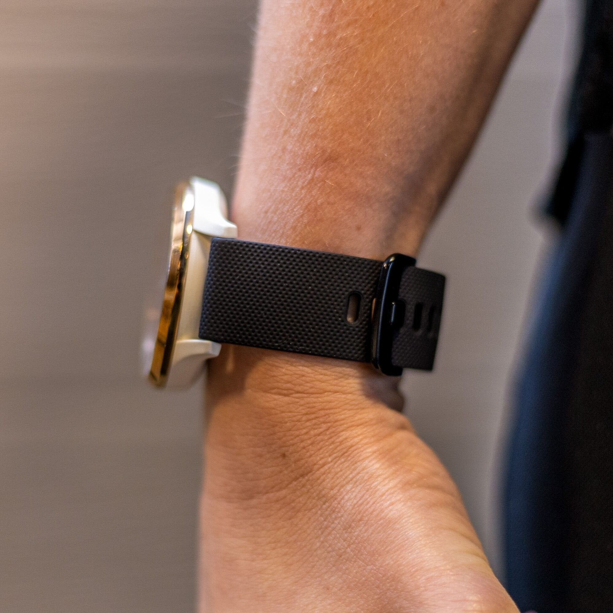Ein Handgelenk mit einer schwarzen Uhr und einem Armband. Die Uhr hat eine goldene Lünette. Der Hintergrund ist unscharf.