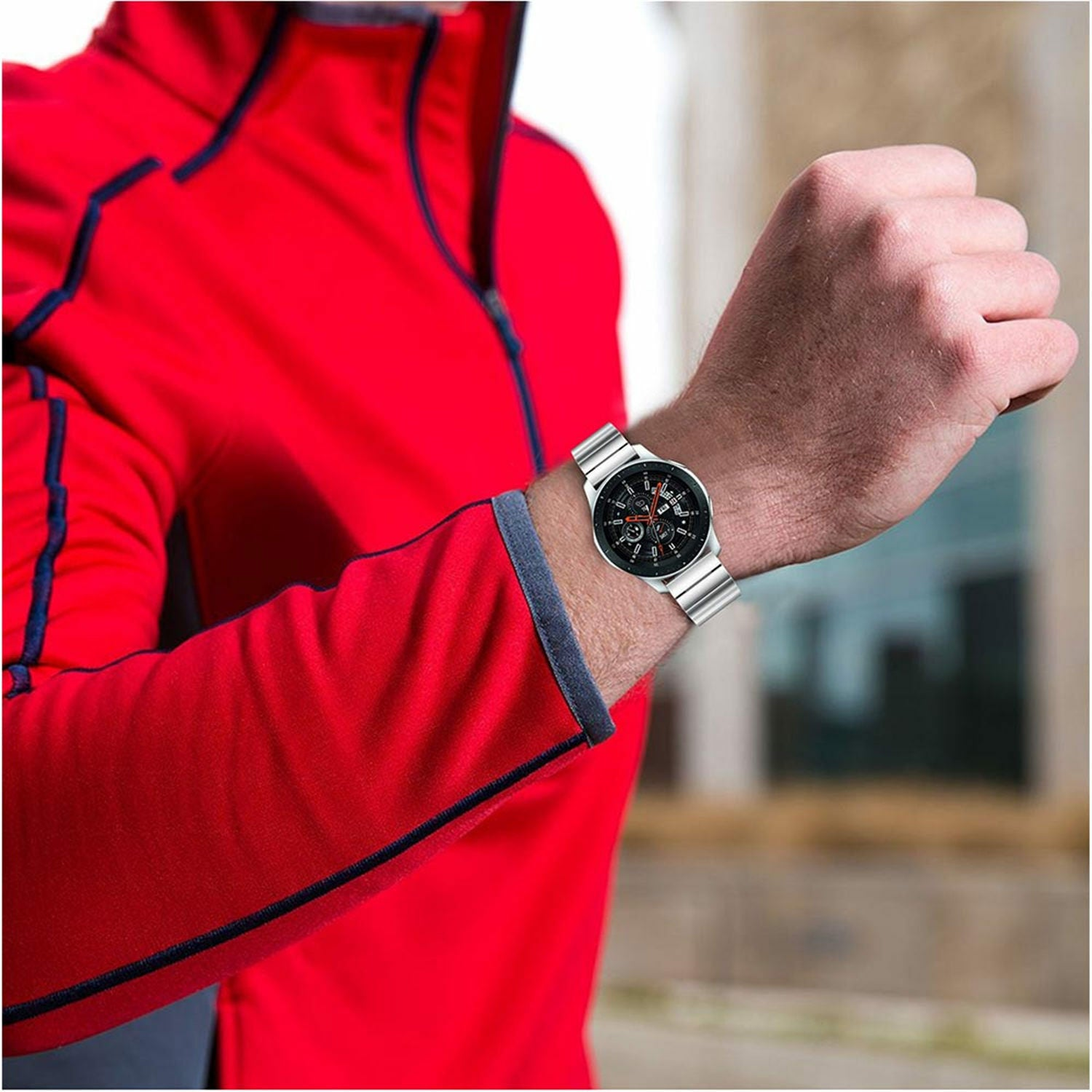 Eine Person trägt eine rote Jacke und eine Uhr. Die Uhr befindet sich am linken Handgelenk. Der Hintergrund ist unscharf.