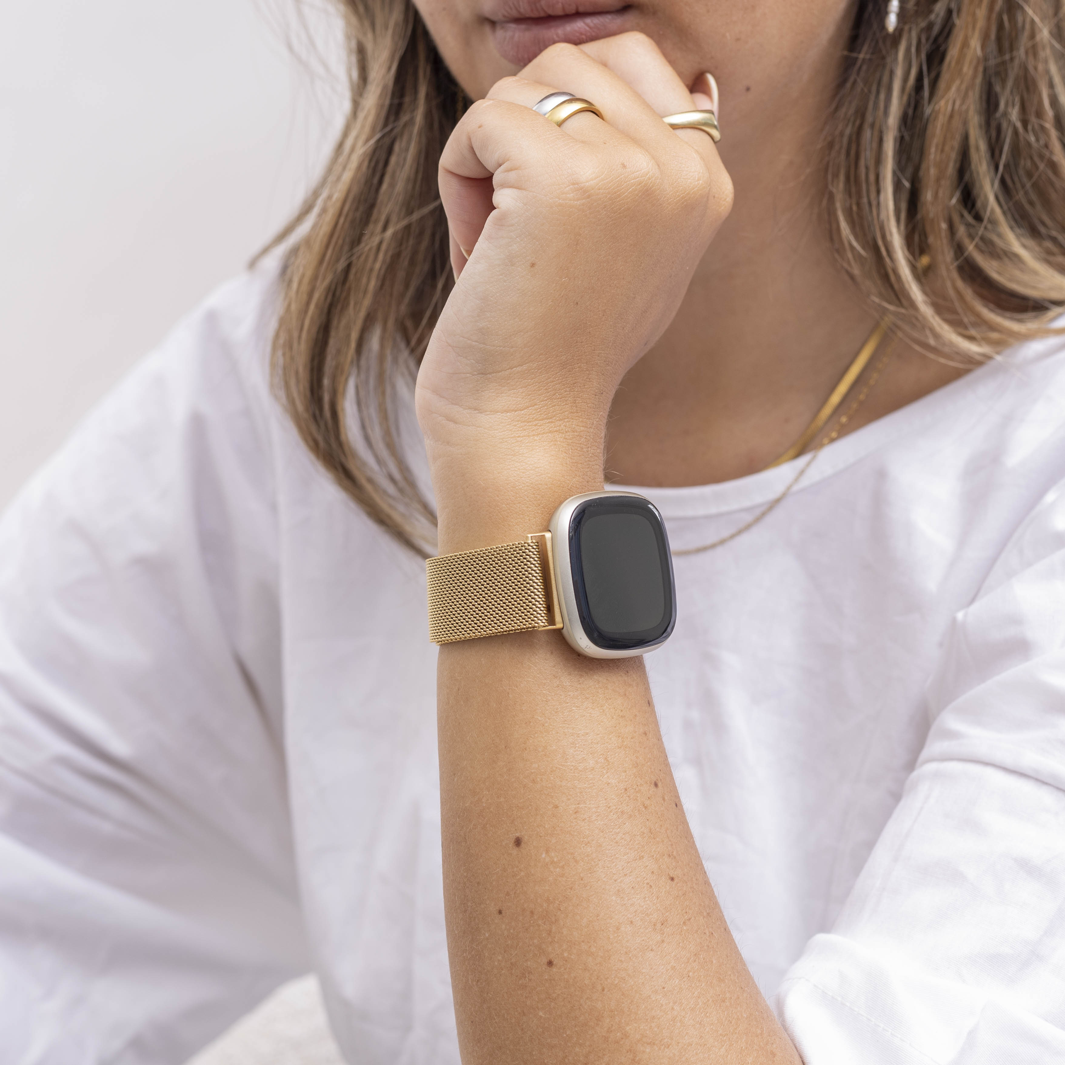 Eine Person, die eine goldene Uhr mit schwarzem Bildschirm trägt. Die Person trägt Ringe und ein weißes Hemd.