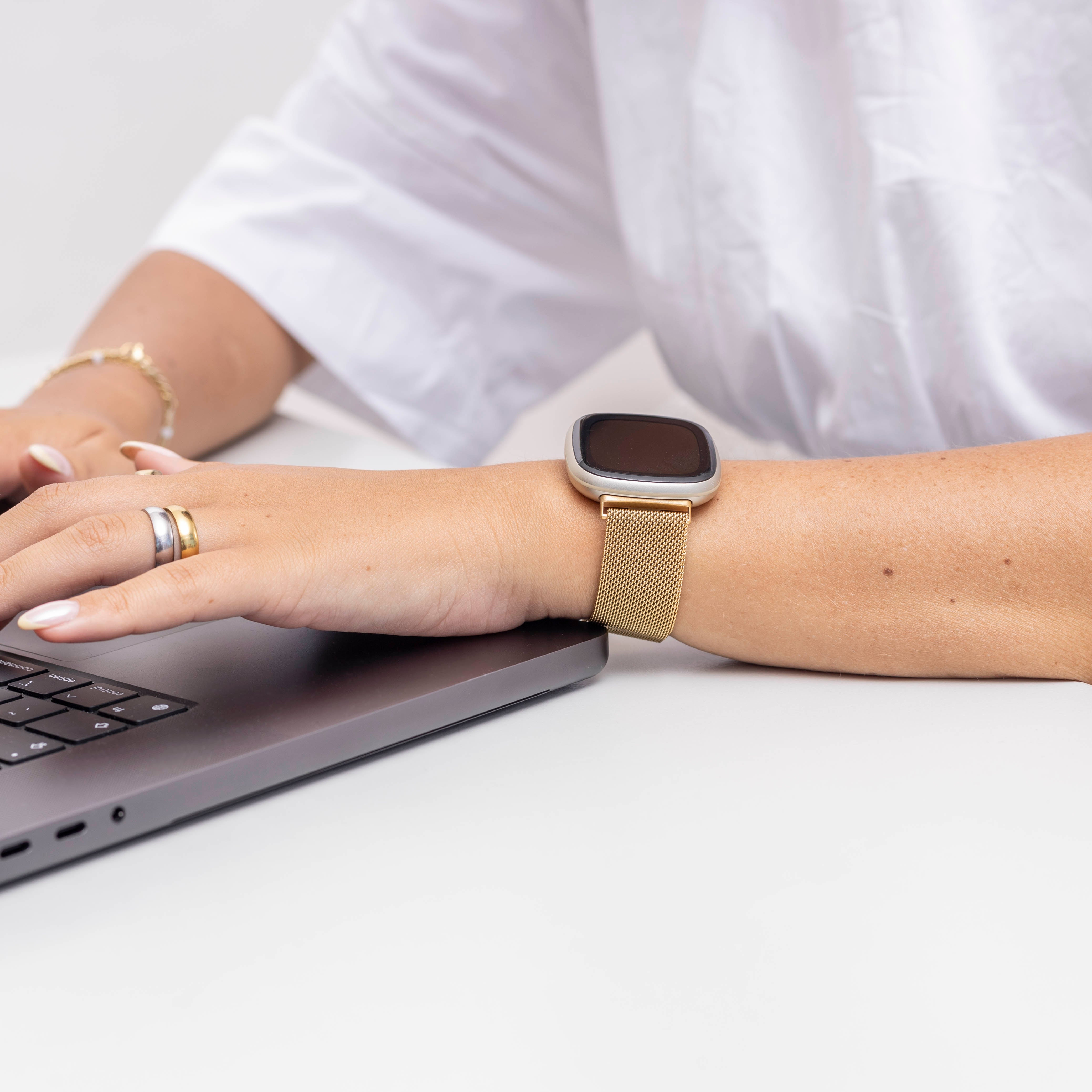 Arm einer Person mit Smartwatch, Ringen und Laptop. Die Person trägt ein weißes Hemd. Weißer Hintergrund.