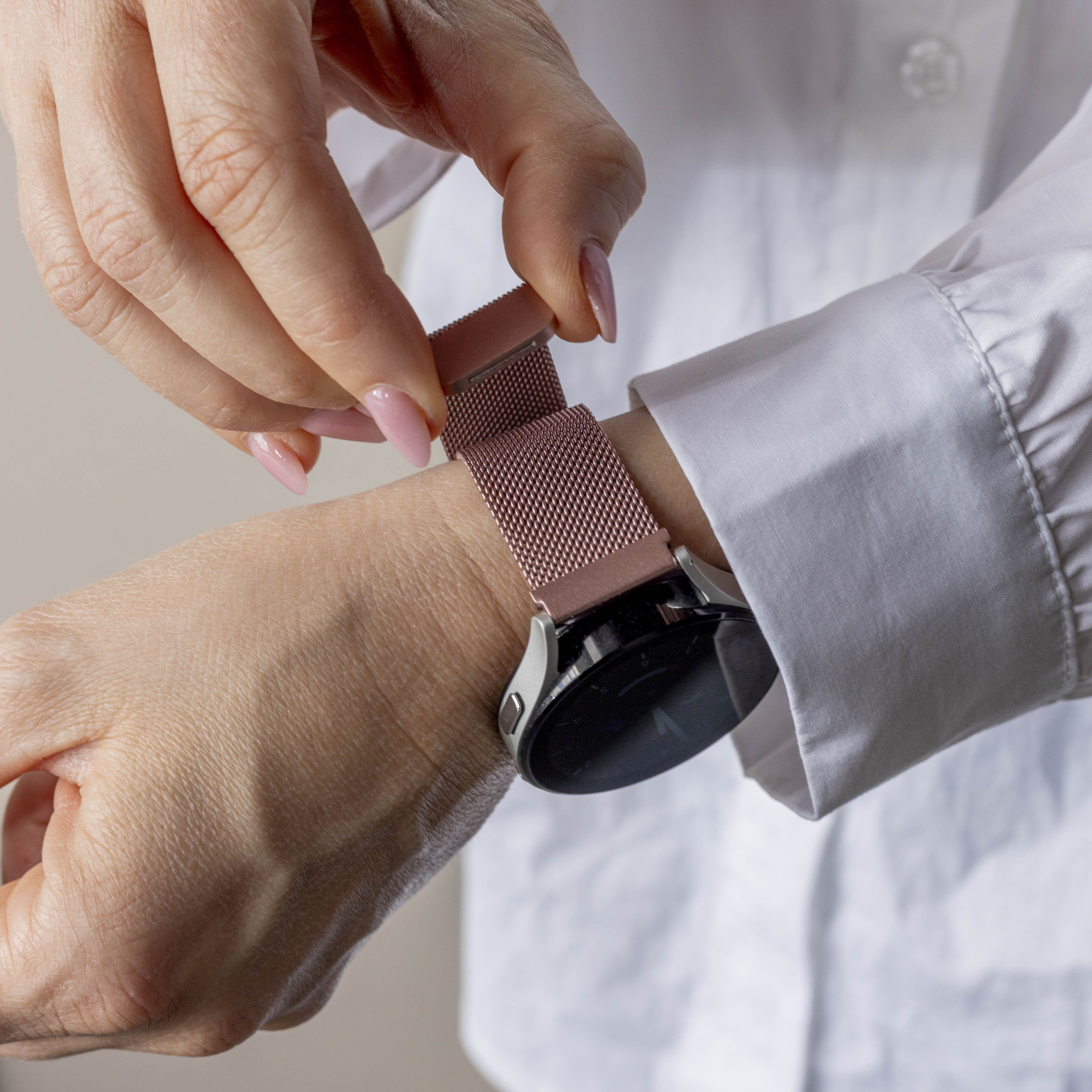 Eine Person passt ein roségoldenes Armband an ihrem Handgelenk an. Weißes Hemd im Hintergrund.