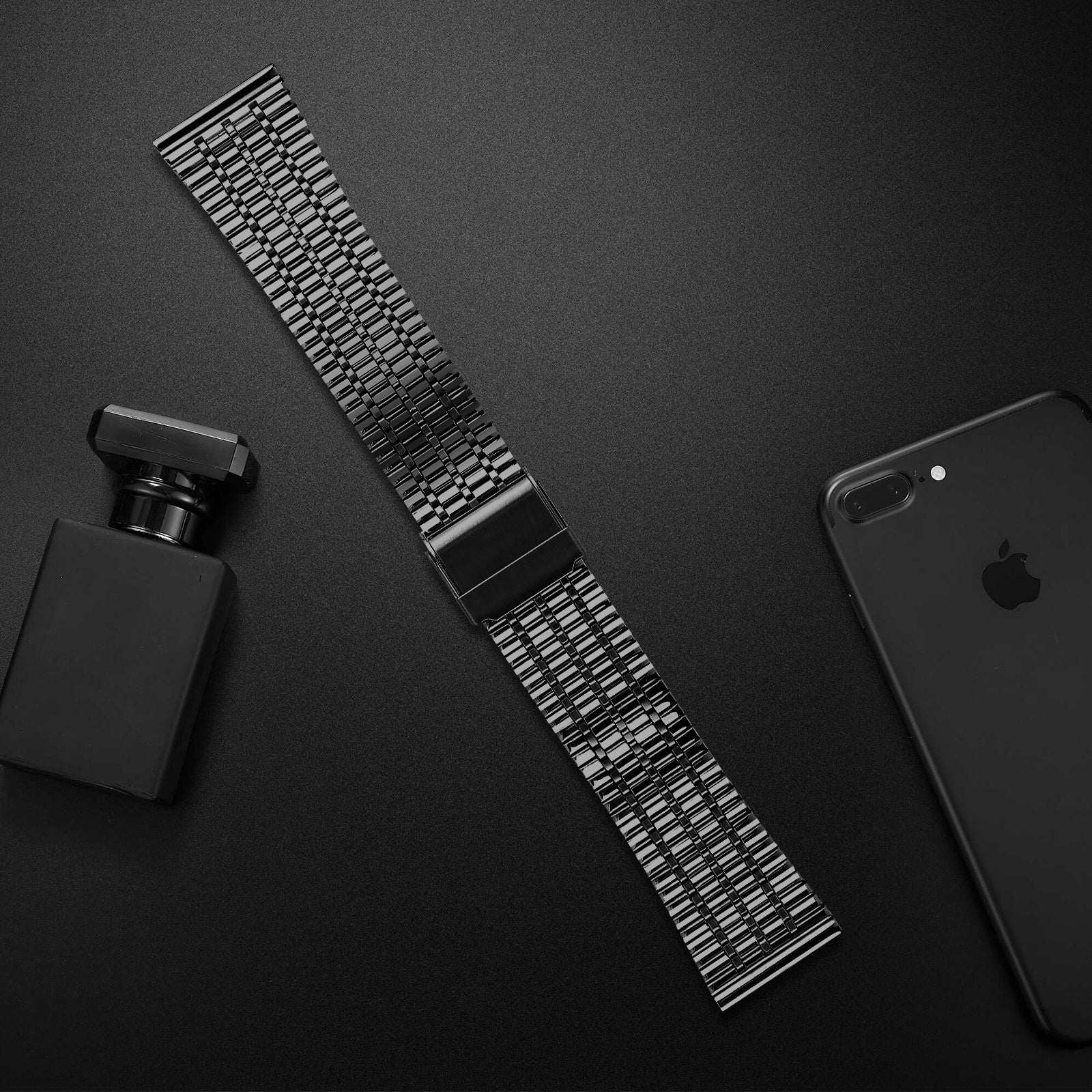Schwarzes Uhrenarmband, Parfümflasche und Telefon auf dunkler Oberfläche.