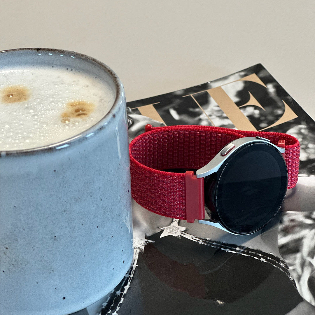 Eine Tasse Kaffee mit Schaum und eine Smartwatch mit rotem Armband auf einem Magazin.