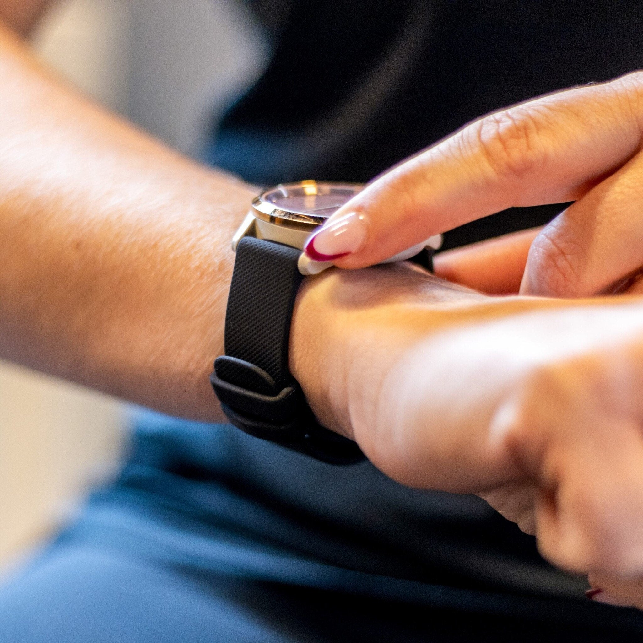 Die Hand einer Person berührt eine Armbanduhr. Die Uhr hat ein schwarzes Band, und die Person hat gepflegte Nägel.