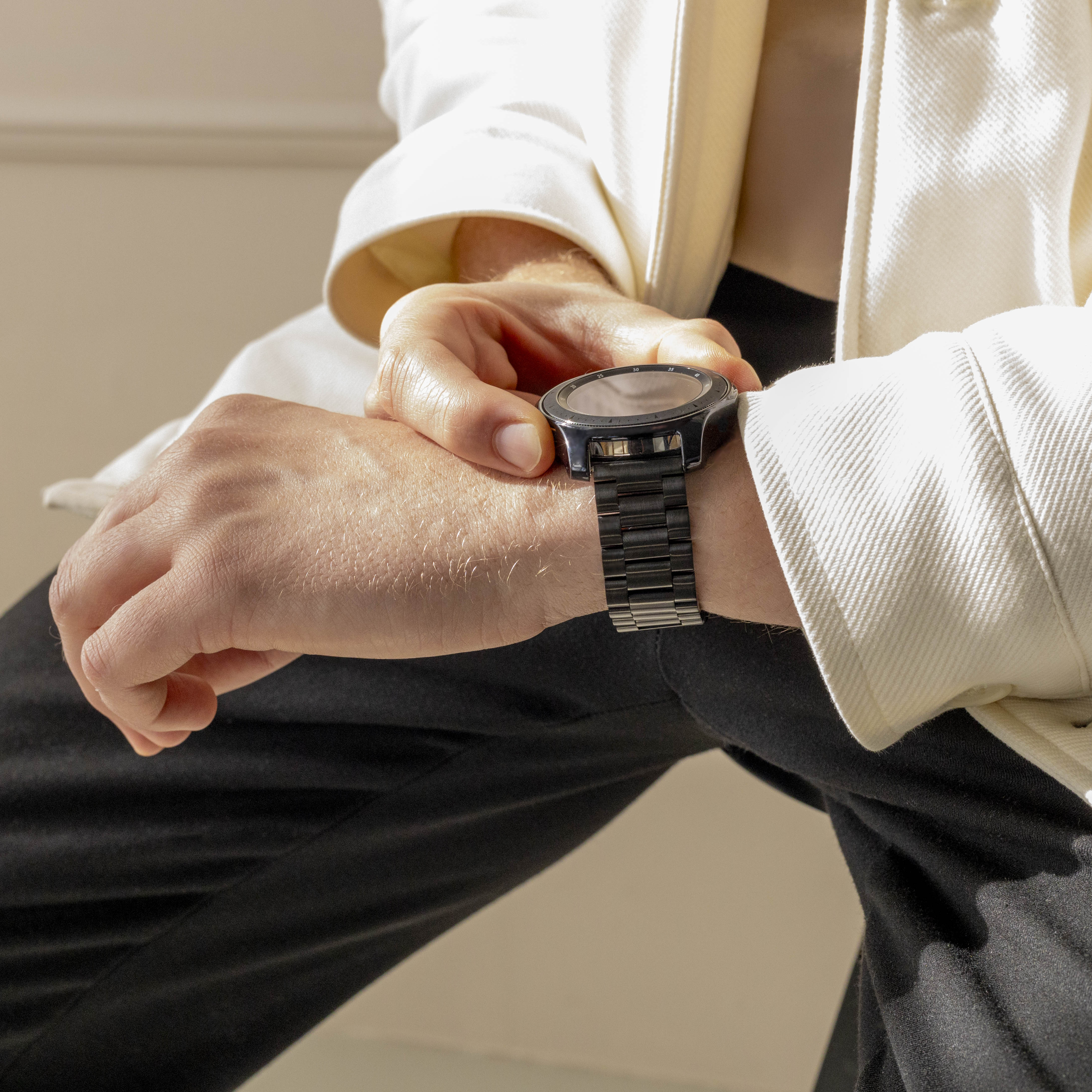 Eine Person in weißer Jacke und schwarzer Hose überprüft eine schwarze Smartwatch am Handgelenk.