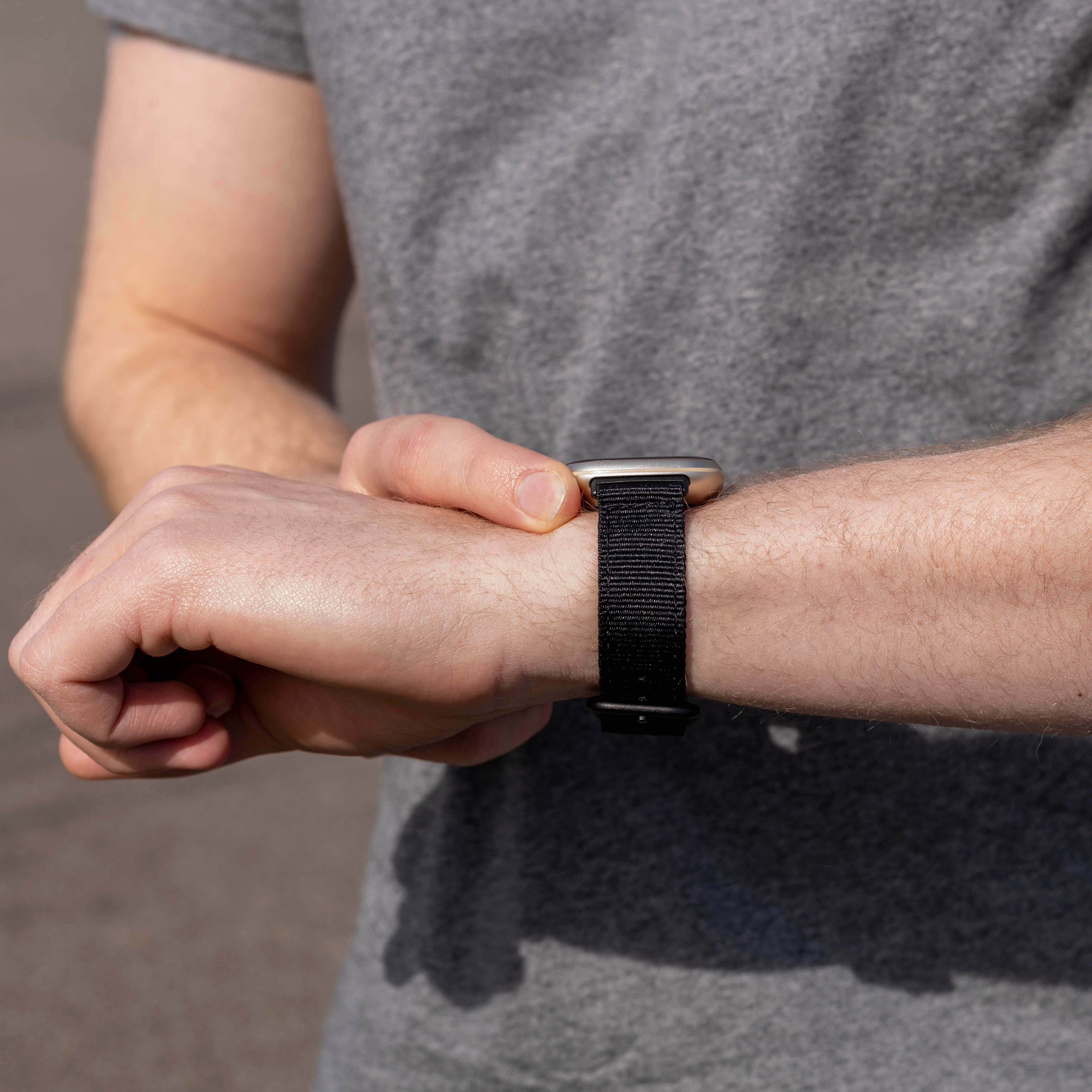 Eine Person in grauem Shirt betrachtet eine Smartwatch am Handgelenk. Die Uhr hat ein schwarzes Armband.