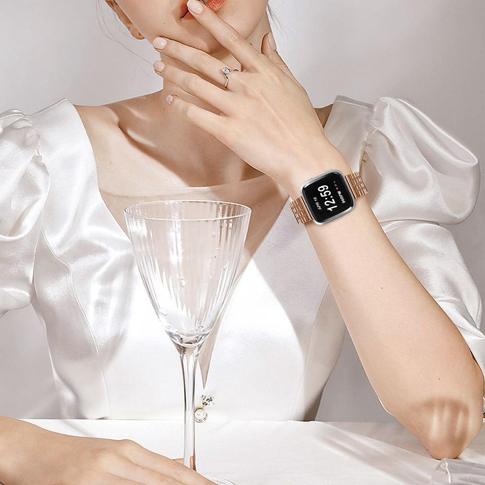Frau im Kleid, Smartwatch am Handgelenk. Ein Weinglas steht auf dem Tisch. Fokus auf die Uhr, die Zeit anzeigt.