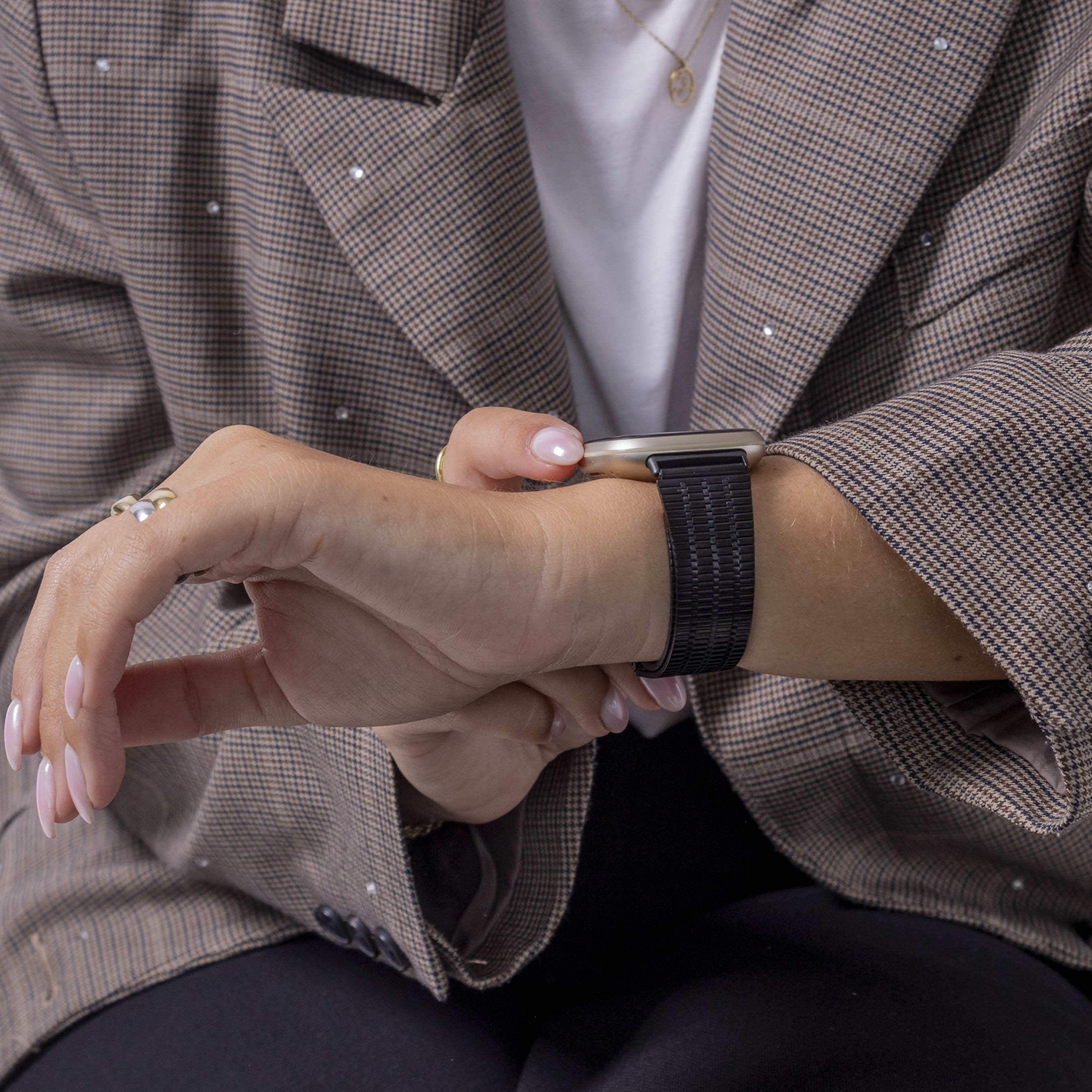 Eine Person, die einen Blazer und eine Uhr trägt. Die Uhr befindet sich am Handgelenk mit einem schwarzen Armband. Die Nägel sind lackiert.