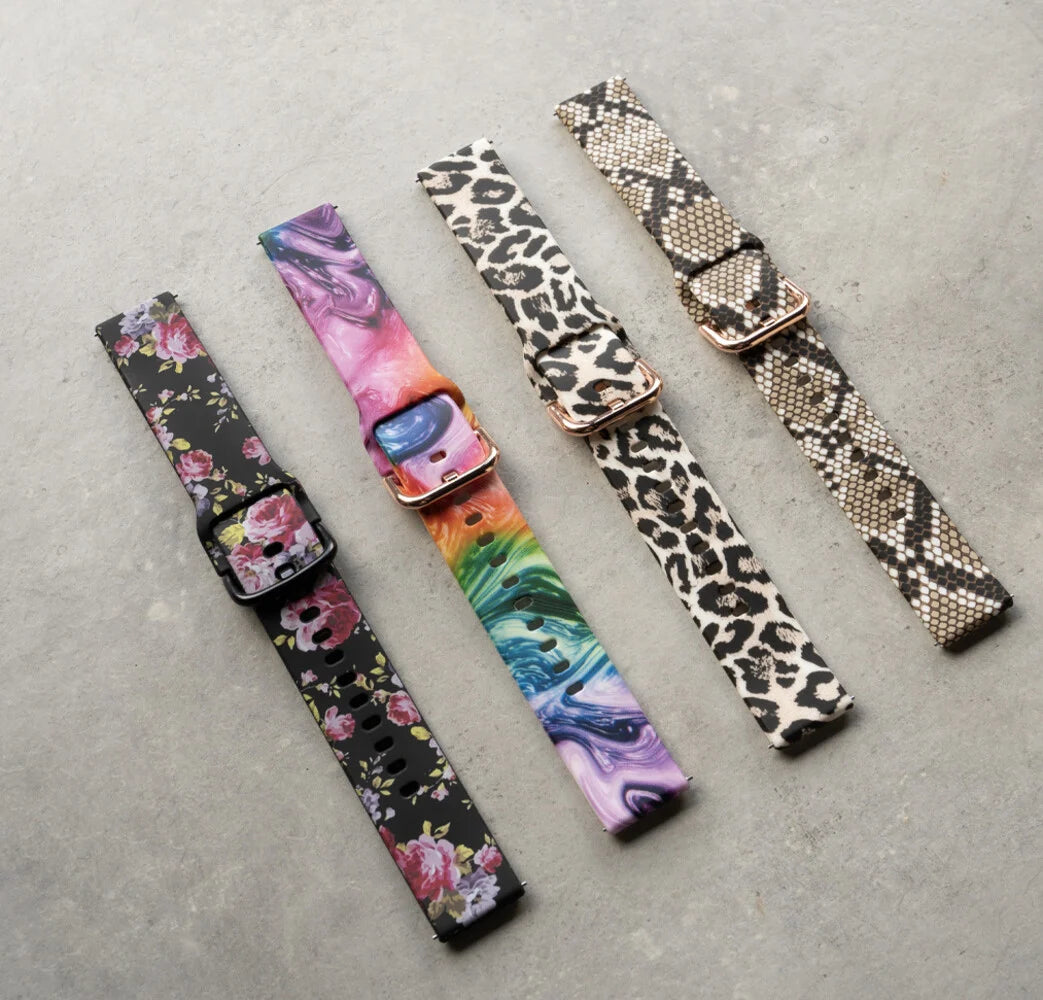 Vier Uhrenarmbänder mit verschiedenen Designs: Blumendruck, bunter Wirbel, Leopardenmuster und Schlangenmuster, auf grauer Oberfläche.