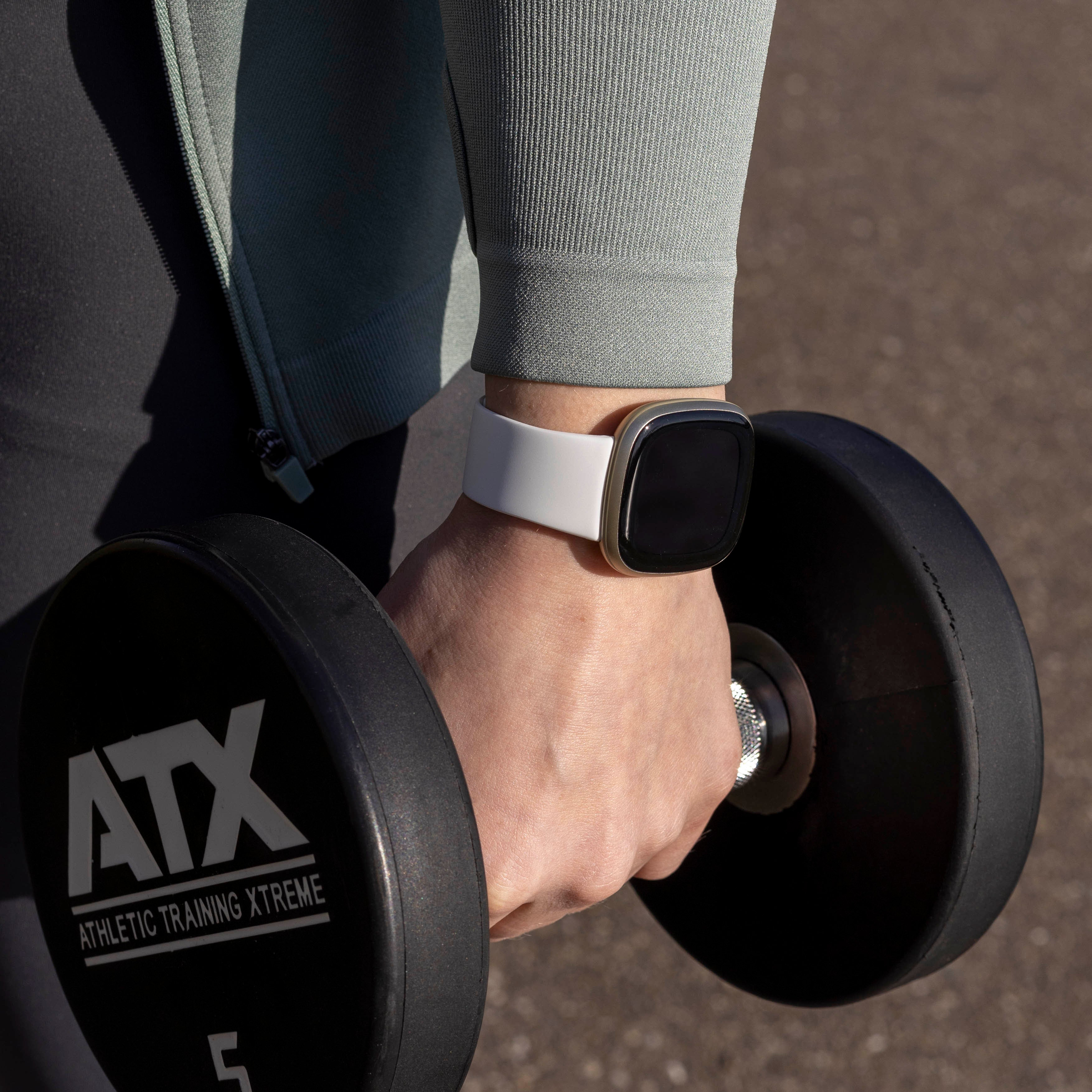 Eine Person, die eine Hantel hält, mit einer Smartwatch am Handgelenk. Die Uhr hat ein weißes Armband und einen schwarzen Bildschirm.