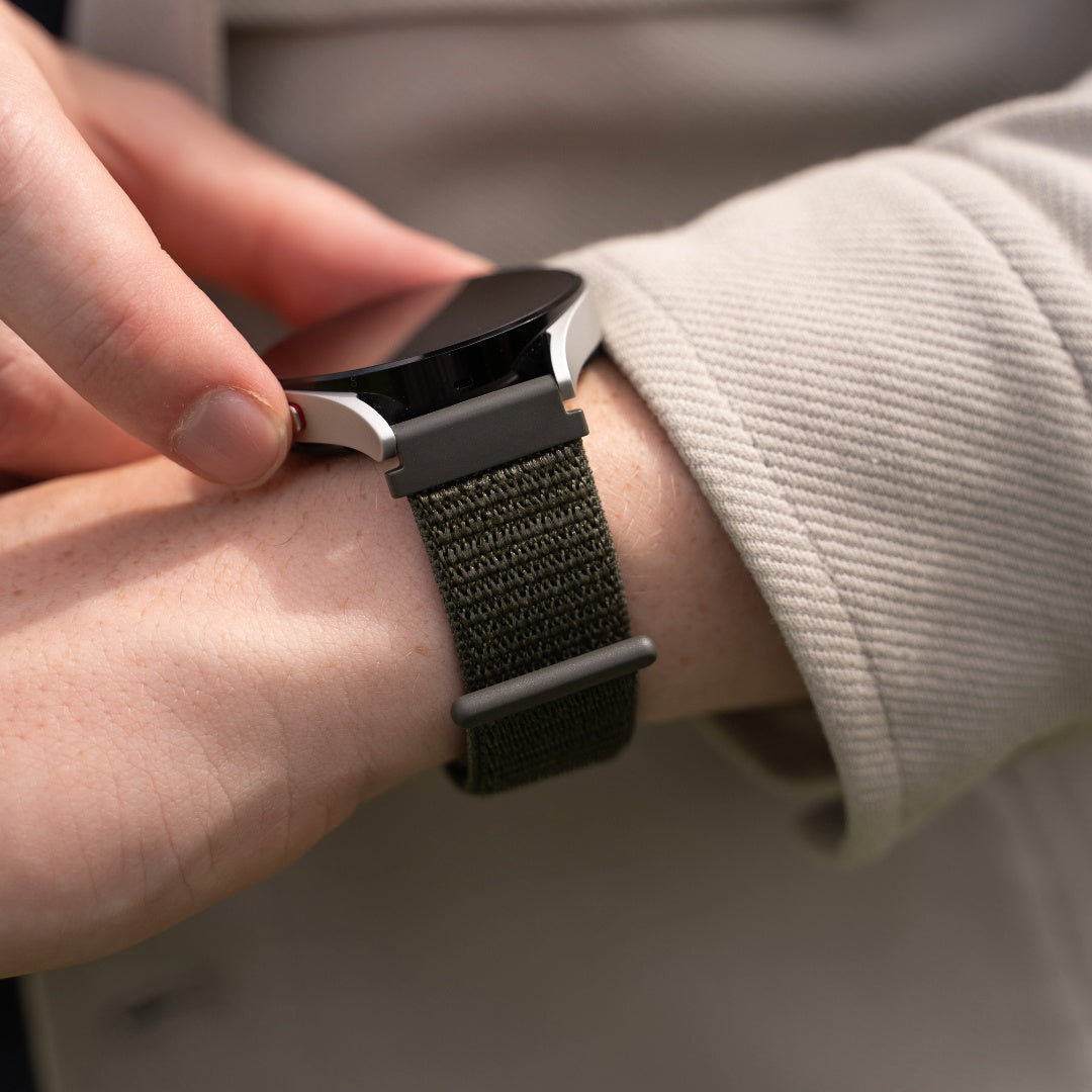 Das Handgelenk einer Person mit einer Smartwatch. Die Uhr hat ein grünes Armband und einen schwarzen Bildschirm.