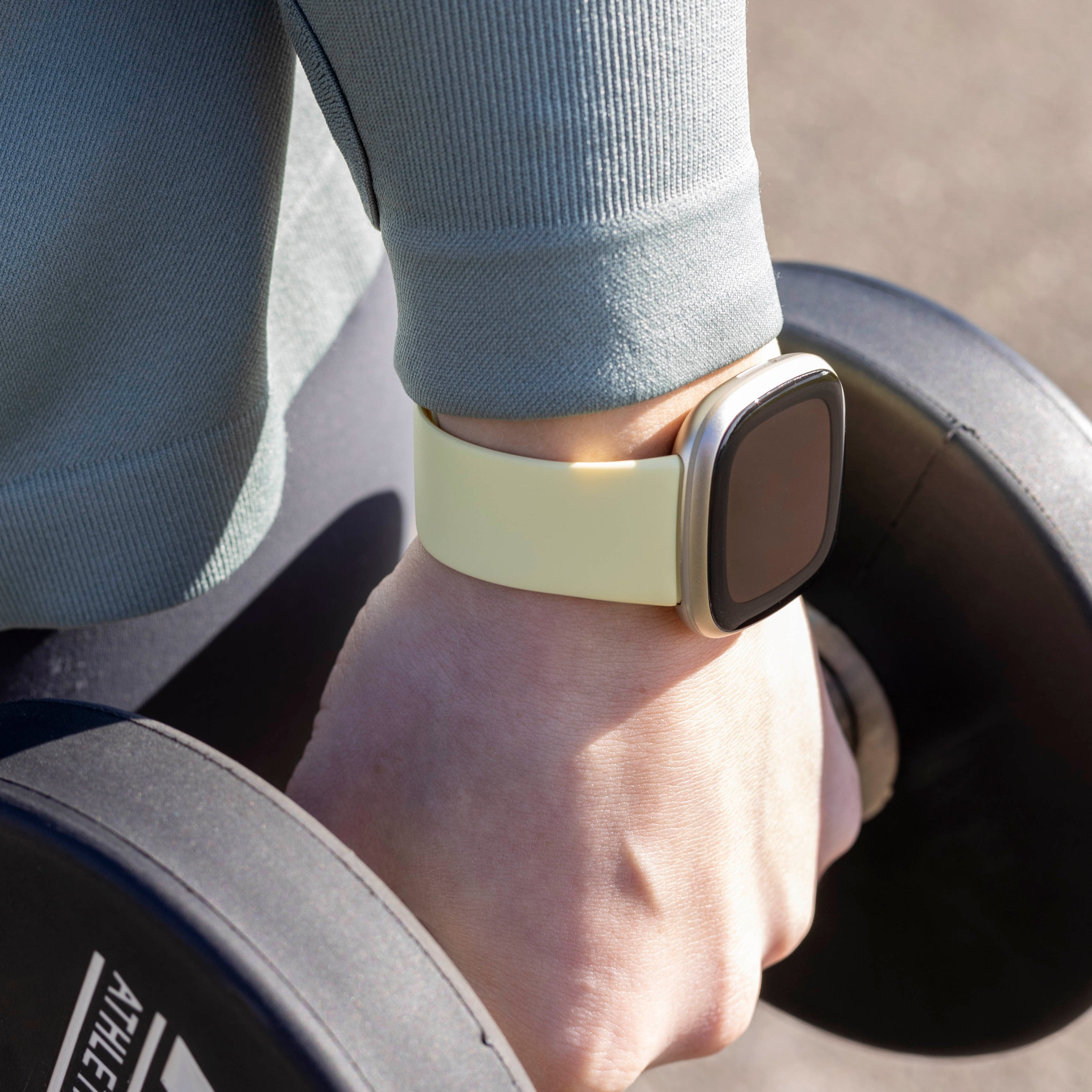 Eine Person, die eine Smartwatch trägt, hält eine Hantel. Die Uhr hat ein gelbes Armband. Die Person trägt ein gr ünes Hemd.