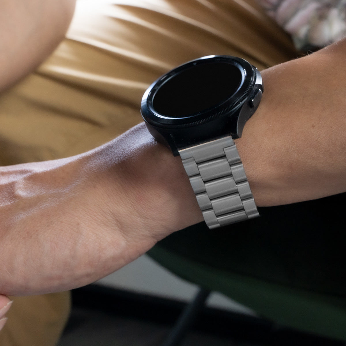 Das Handgelenk einer Person mit einer schwarzen Smartwatch mit Metallarmband. Die Uhr hat einen dunklen Bildschirm. Der Hintergrund ist unscharf.