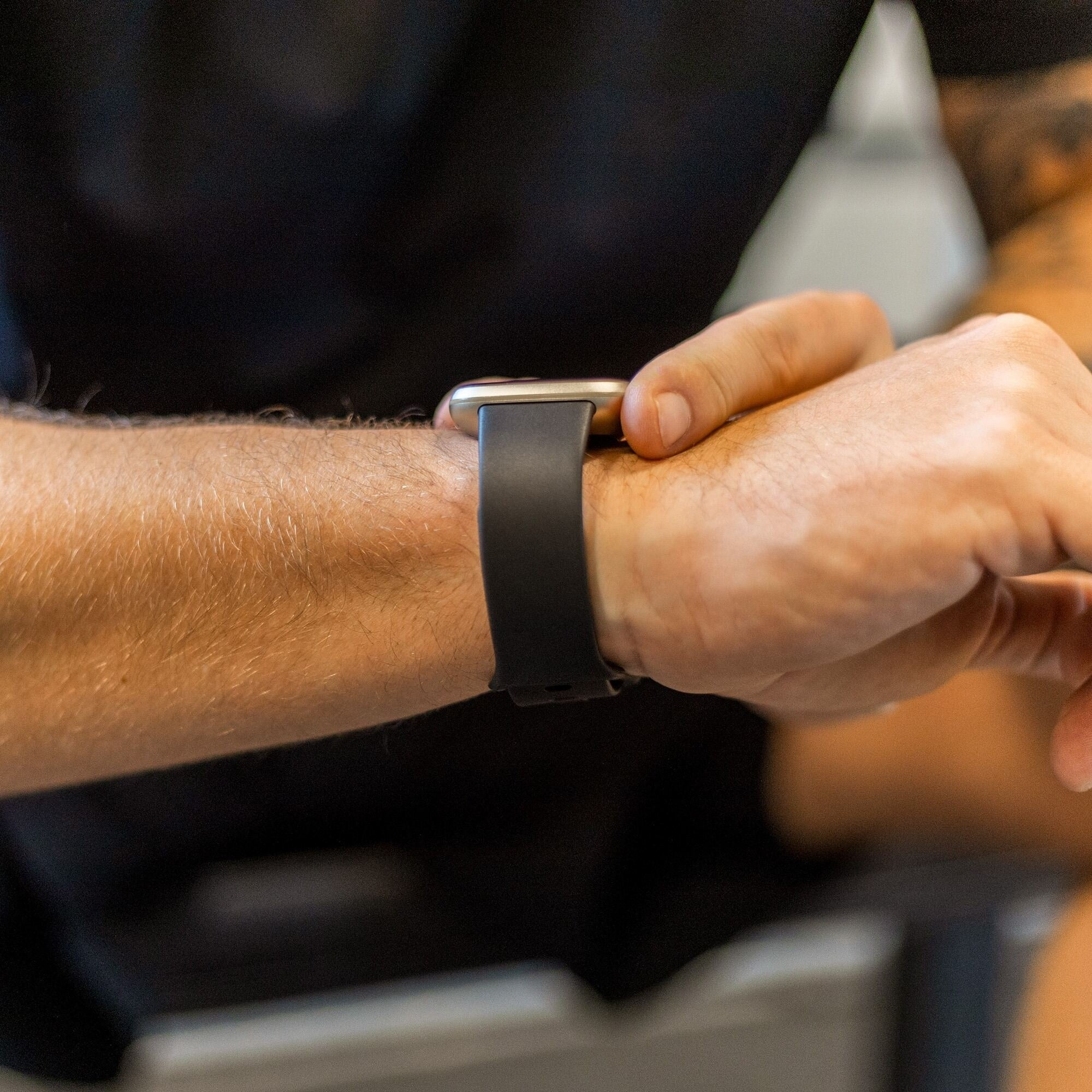 Ein Arm mit einer schwarzen Smartwatch. Die Person trägt ein schwarzes Hemd. Das Uhrenarmband ist schwarz.