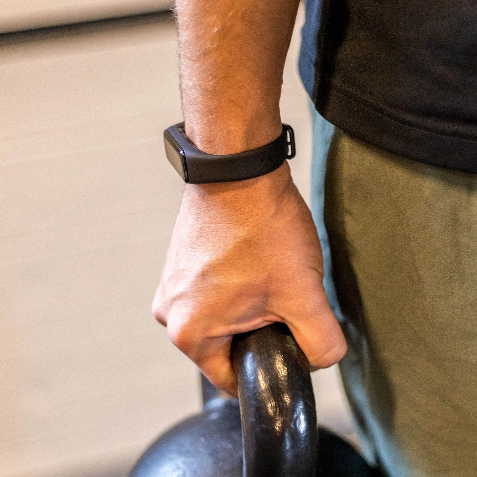 Eine Hand hält eine schwarze Kettlebell. Eine schwarze Smartwatch befindet sich am Handgelenk der Person. Die Person trägt ein schwarzes Hemd.