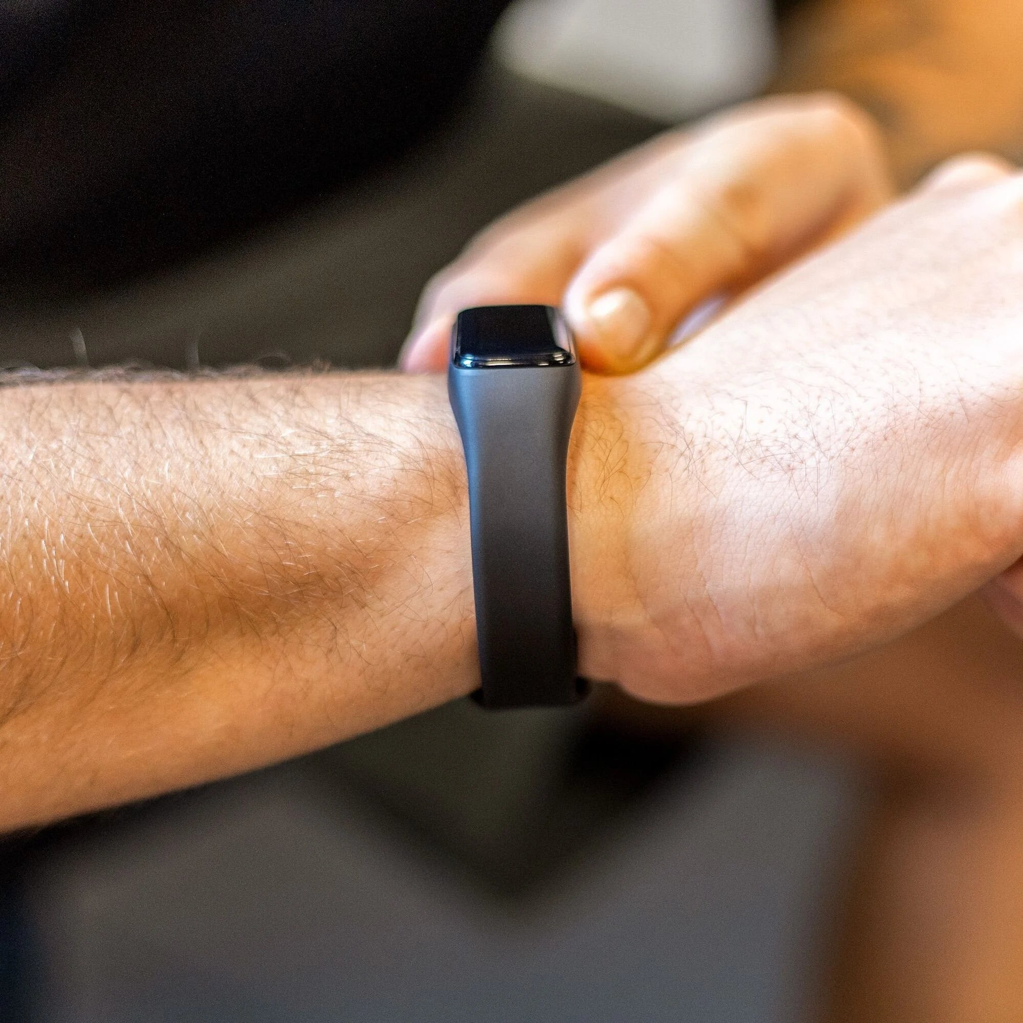 Das Handgelenk einer Person mit einem schwarzen Fitness-Tracker. Die Person benutzt die andere Hand, um den Tracker einzustellen.